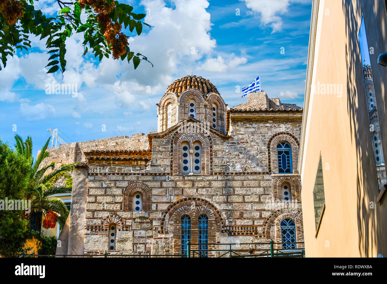 Un antica chiesa greca nel quartiere Plaka di Atene Grecia con l'antica acropoli collina alle spalle come turista a godere le viste sotto la bandiera Foto Stock