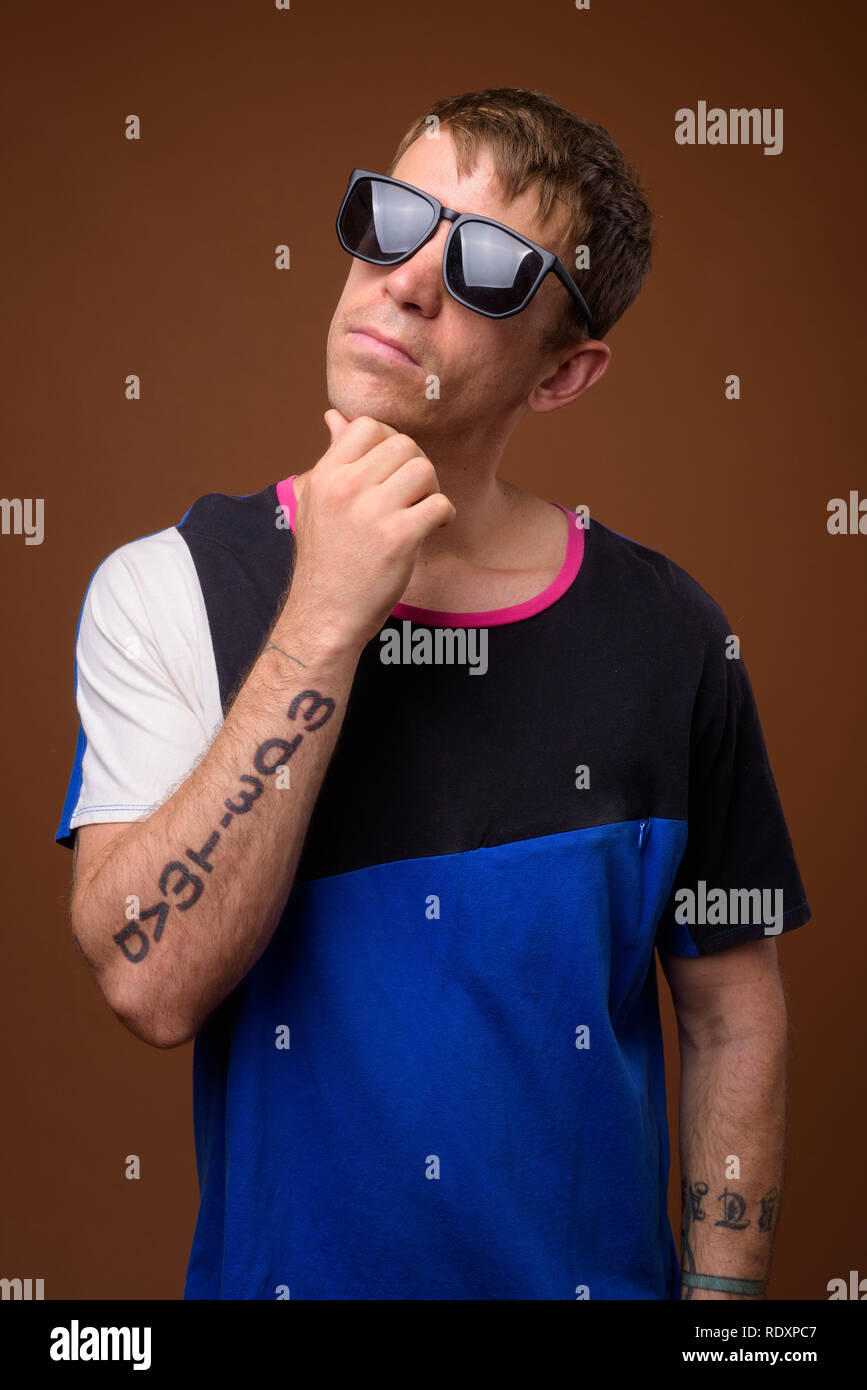 Uomo che indossa maglietta blu e occhiali da sole contro lo sfondo marrone Foto Stock