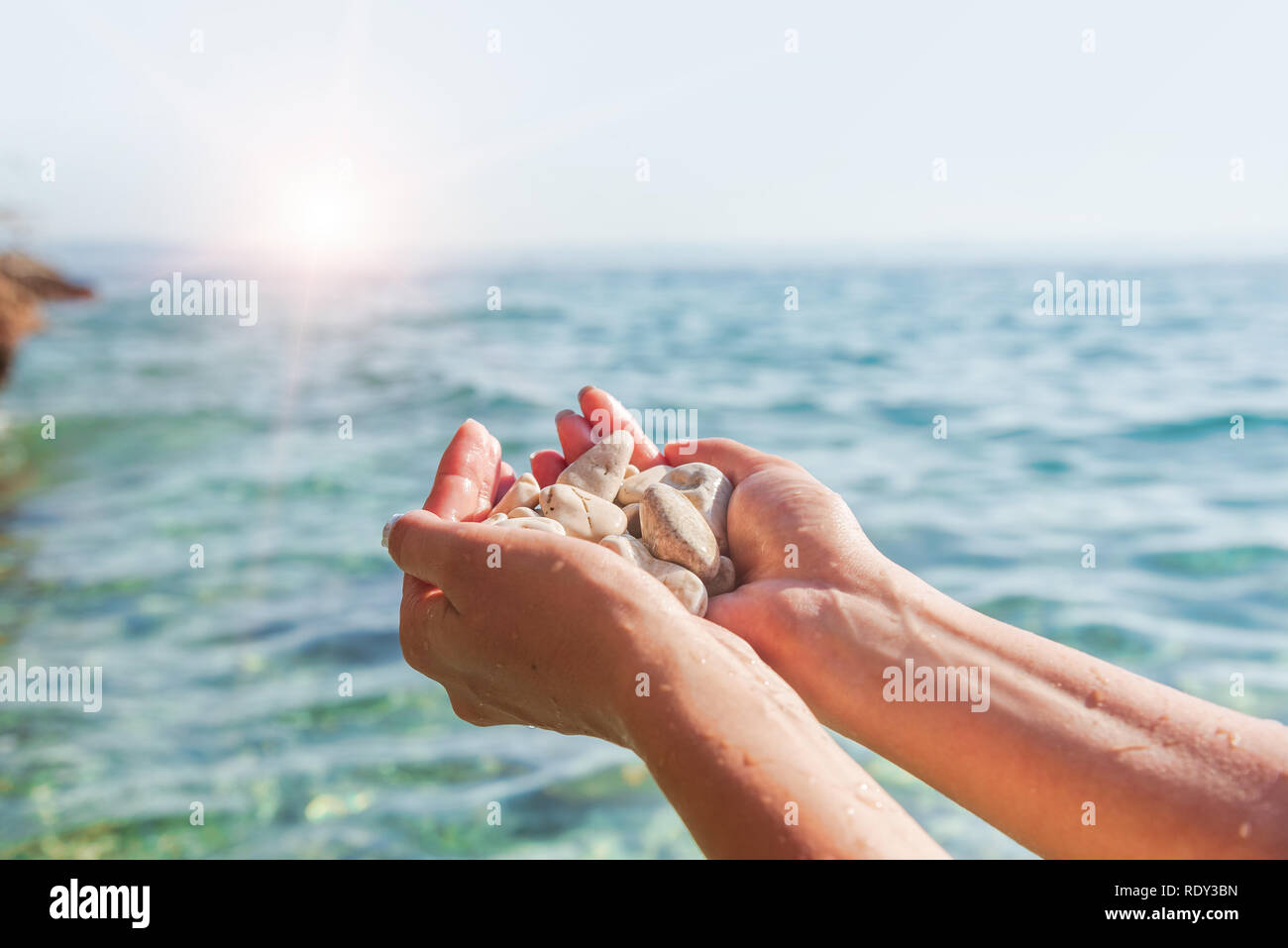 Mani femminili sullo sfondo del mare o oceano sono azienda pietre di mare. Foto Stock