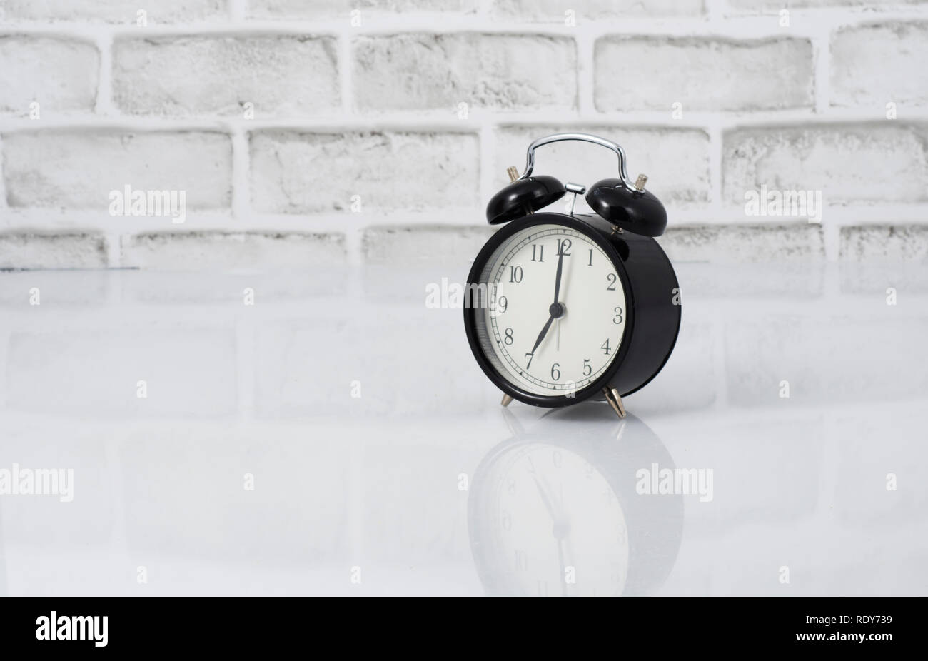 Un vintage nero orologio sveglia lettura 7 am su un bianco muro di mattoni in background Foto Stock