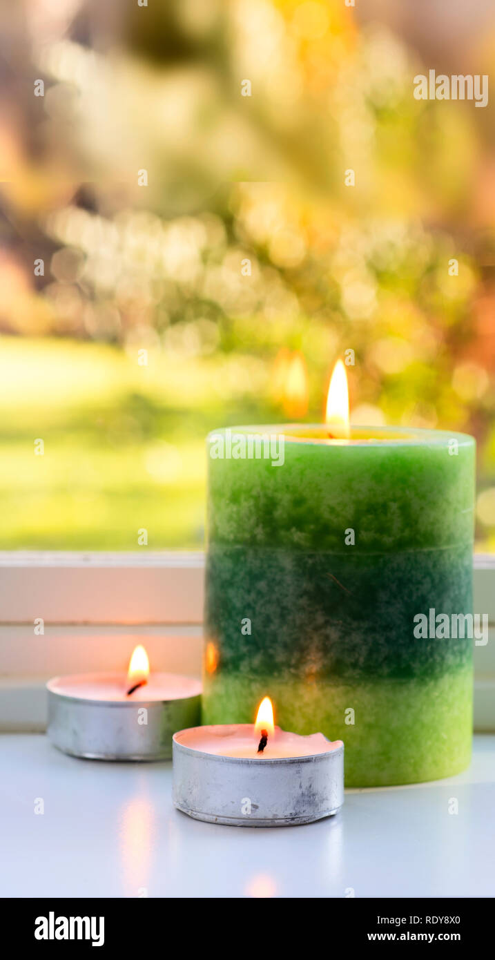 Un ampio e verde candela e due tealight sono la masterizzazione su un davanzale con luminosi colori dell autunno in background Foto Stock