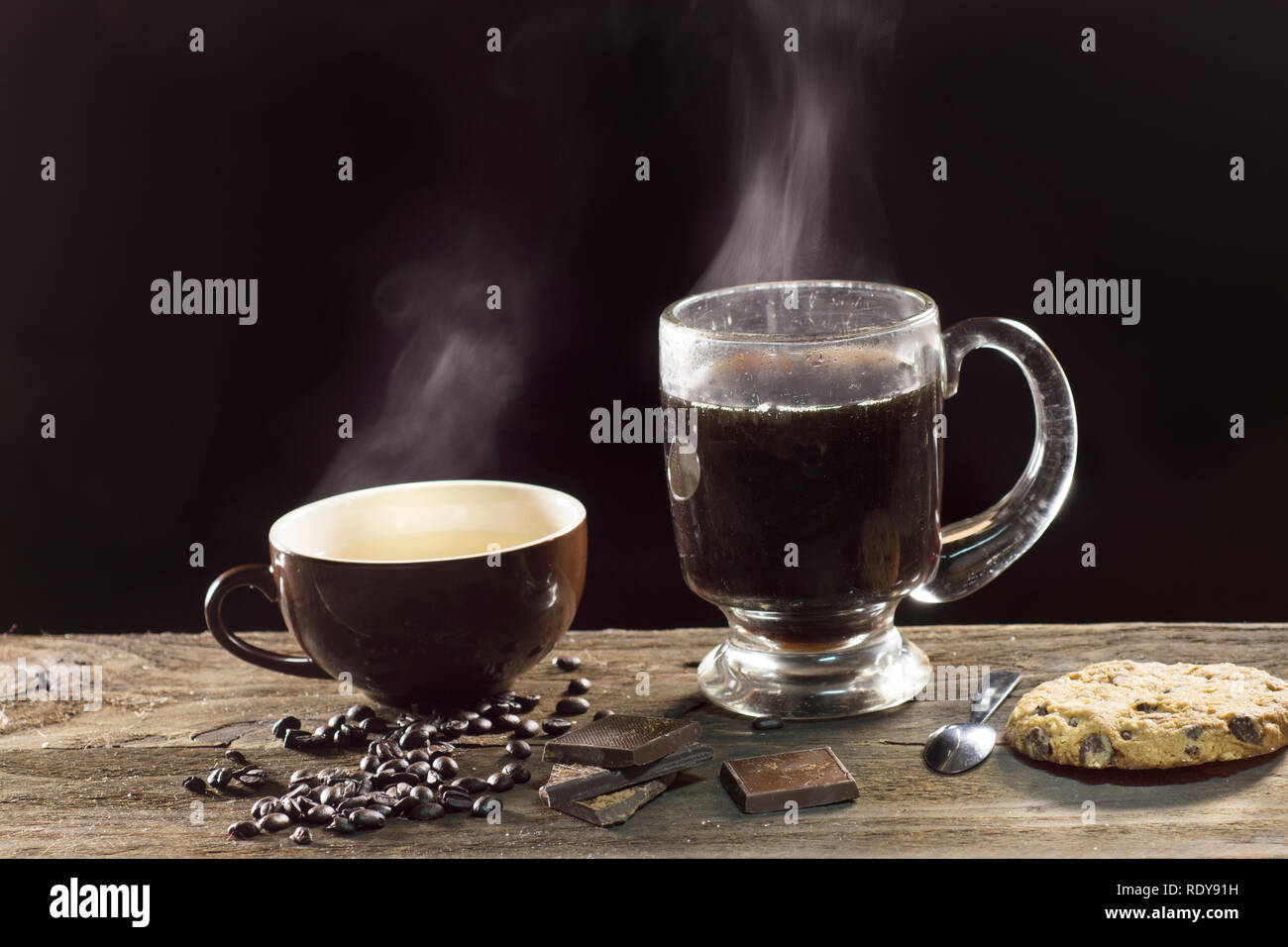 Cottura a vapore di due tazze di caffè sul fondo scuro, con i chicchi di caffè e pezzi di cioccolato Foto Stock