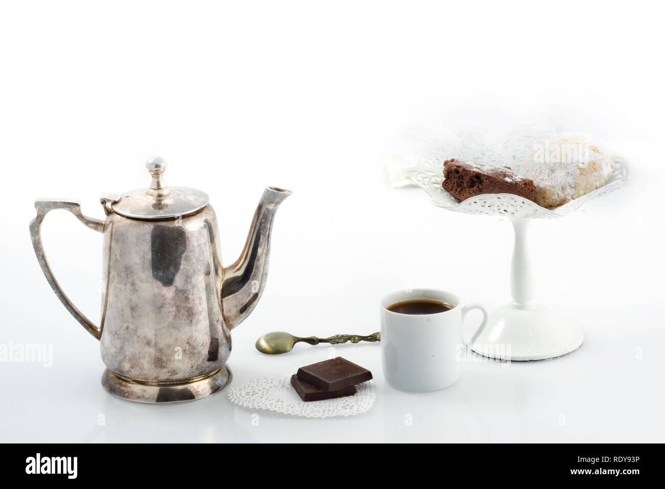 Un vintage peltro caffettiera, una tazza di caffè e un piedistallo bianco con dolci su sfondo bianco Foto Stock