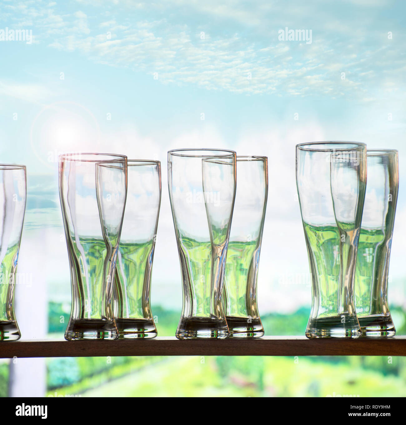 Pulire gli occhiali per acqua o birra, in piedi su un ripiano da una grande finestra con vegetazione e cielo visibili attraverso di loro. Spazio per il testo. Foto Stock