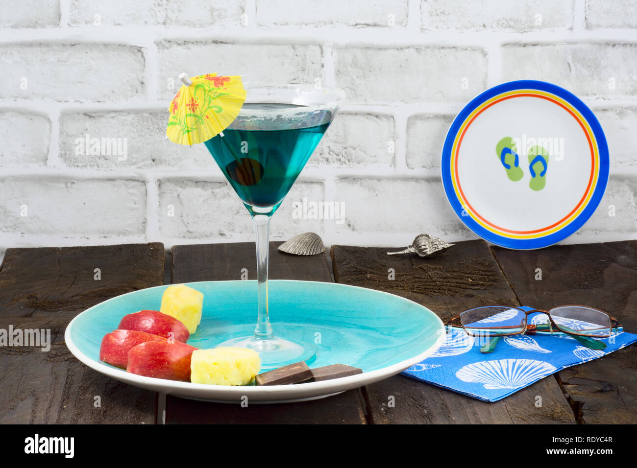 Simboli della vacanza - un martini drink con un ombrello, un piatto di frutta, immagini di gusci e sandali Foto Stock