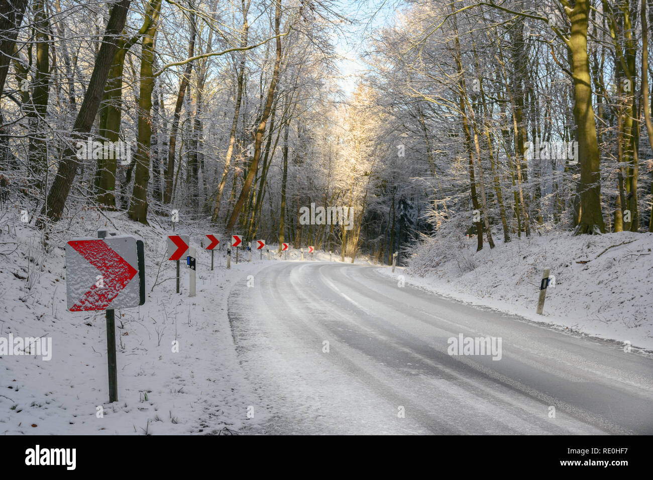 Segnaletica con frecce rosse su una curva pericolosa in un paese nevoso la strada attraverso il bosco invernale, sicurezza concetto guida, spazio di copia Foto Stock