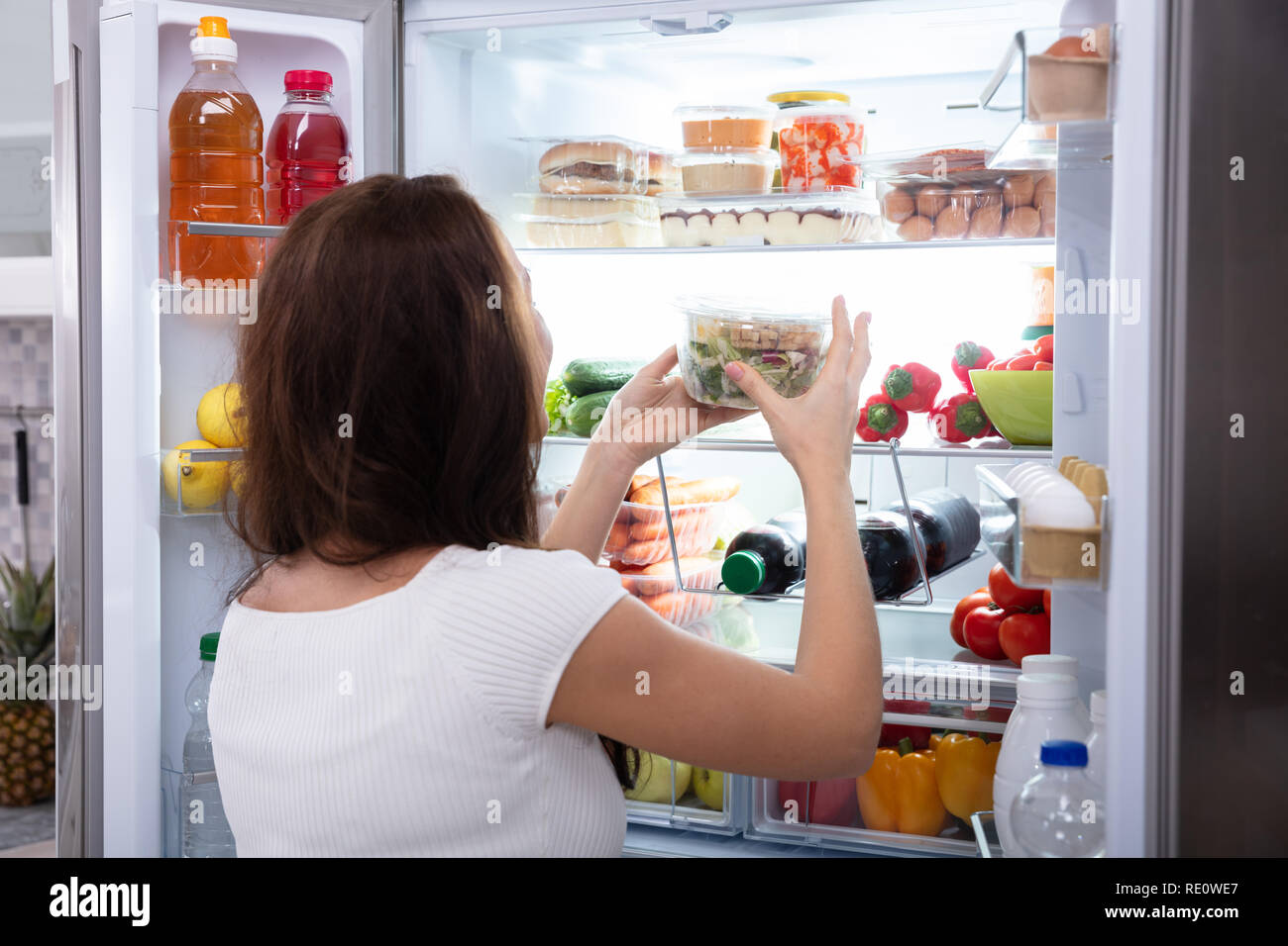 Vista posteriore di una giovane donna prendendo il cibo dal frigorifero Foto Stock