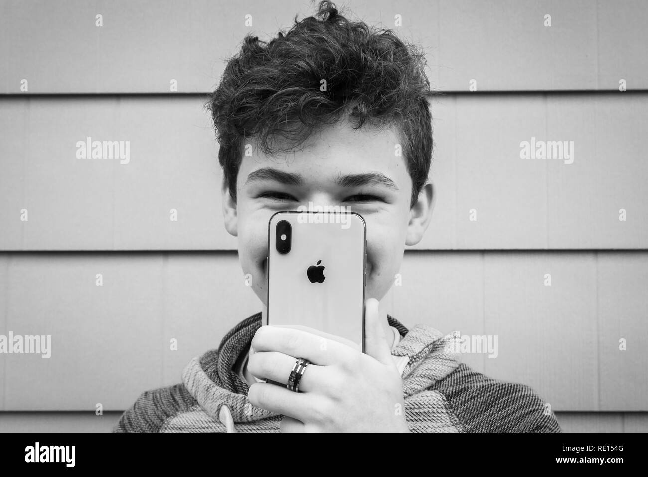 Adolescente di sesso maschile che sorregge il nuovo iPhone X davanti al suo volto e un grande sorriso Foto Stock