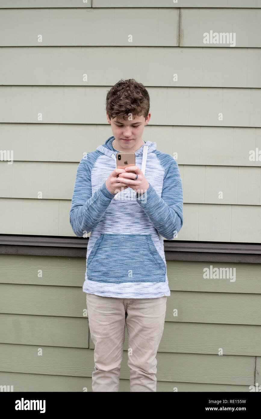 Ragazzo adolescente texting sul suo nuovo Apple iPhone x Foto Stock