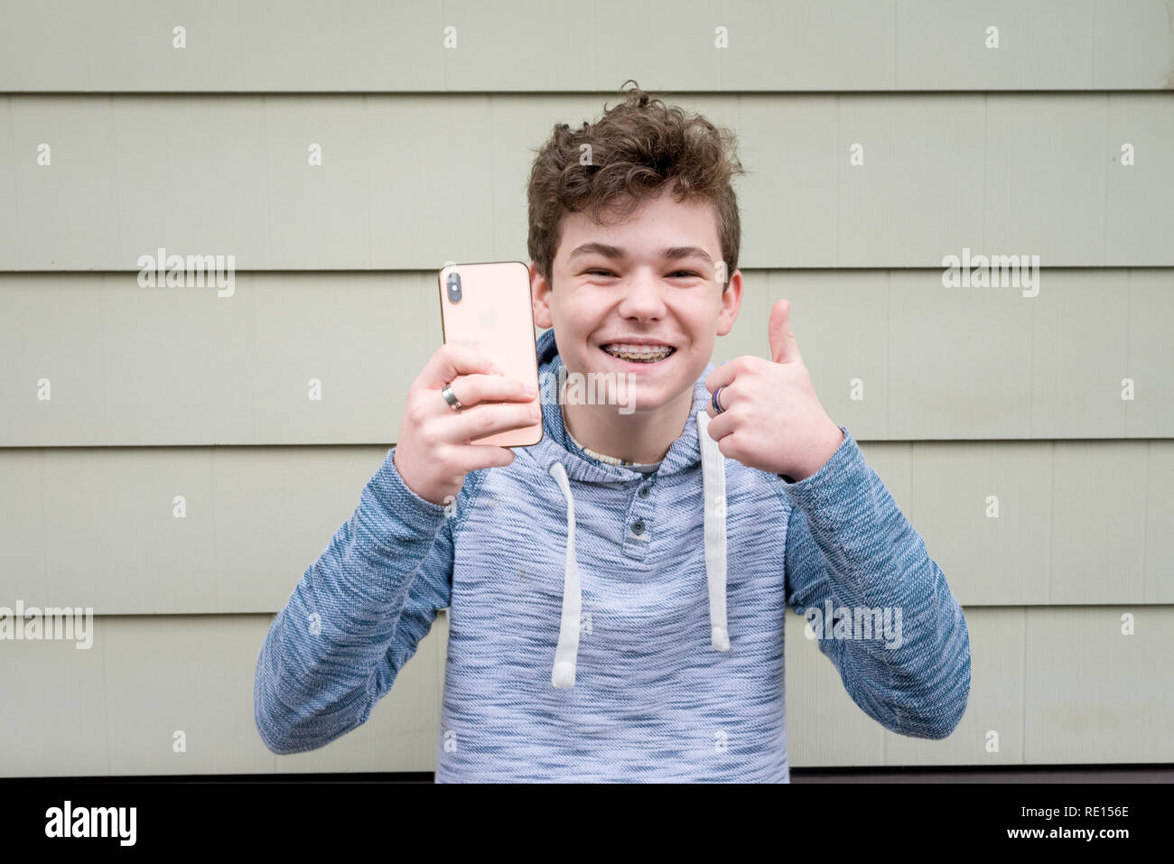 Adolescente di sesso maschile dando pollice in su mentre si tiene il suo nuovo Apple iPhone x Foto Stock