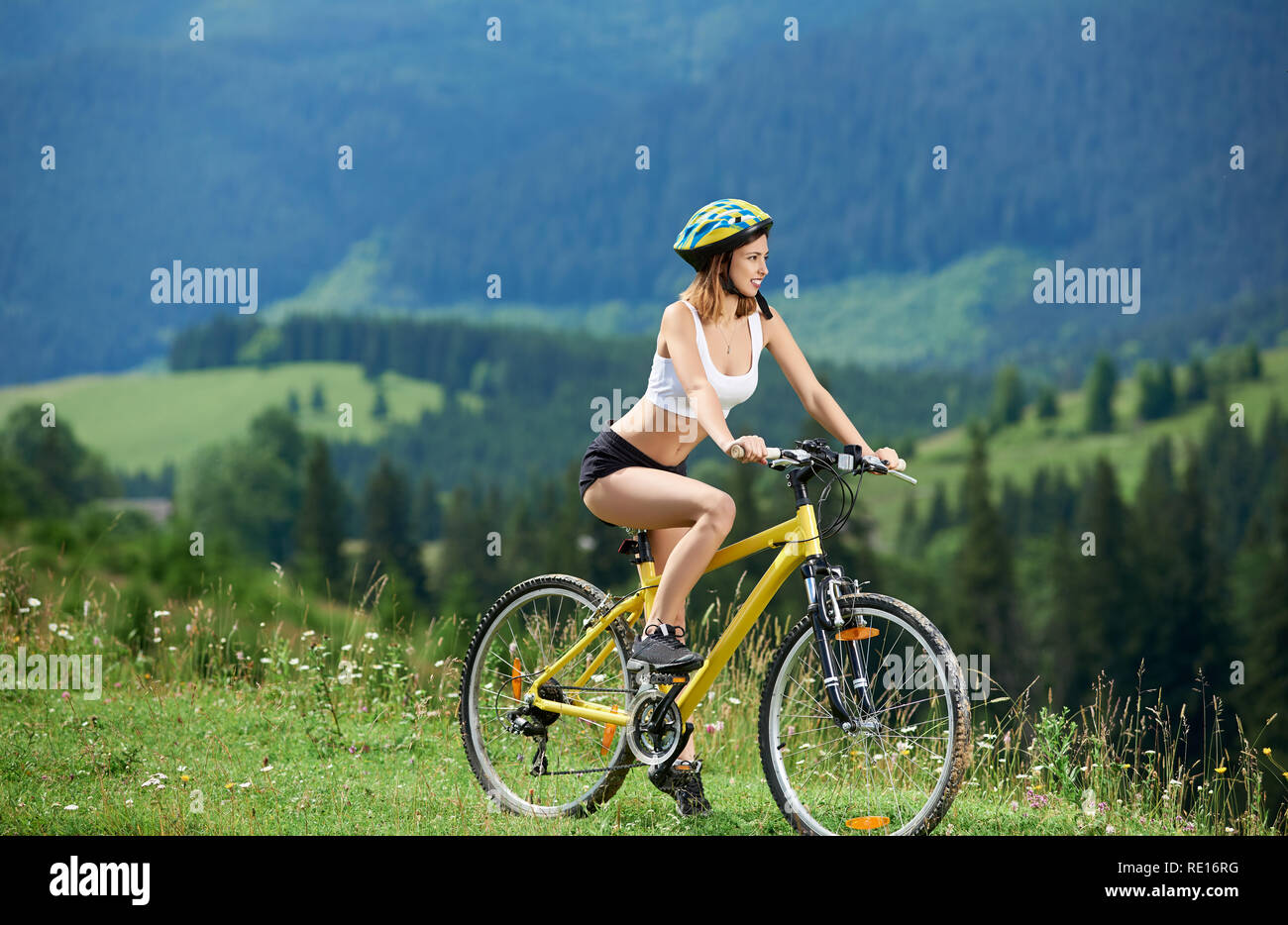 Bella femmina sportivo ciclista ciclismo su giallo moto su un sentiero rurale in montagna, indossando il casco, godendo della vista della valle sulla giornata di sole. Montagne, foreste sullo sfondo. Outdoor sport attività Foto Stock