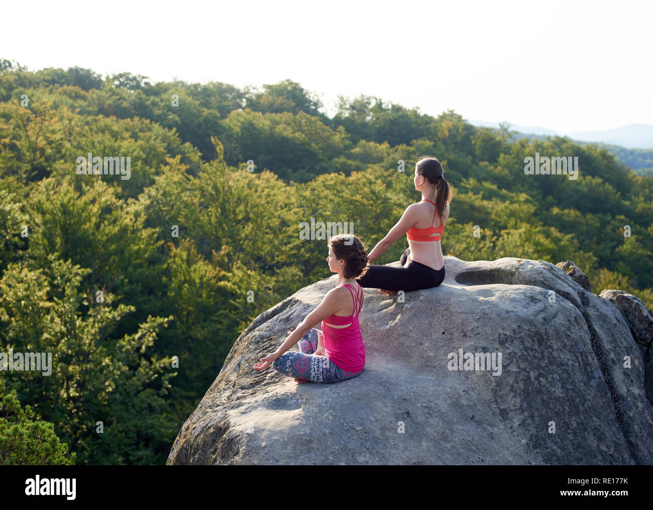 Vista dall'alto di due athletic nudi di donne in seduta lotus pongono sulla sommità di enormi rocce di montagne verdi e cielo blu chiaro dello sfondo. Lo Yoga, fitness e uno stile di vita sano concetto. Siddhasana Foto Stock