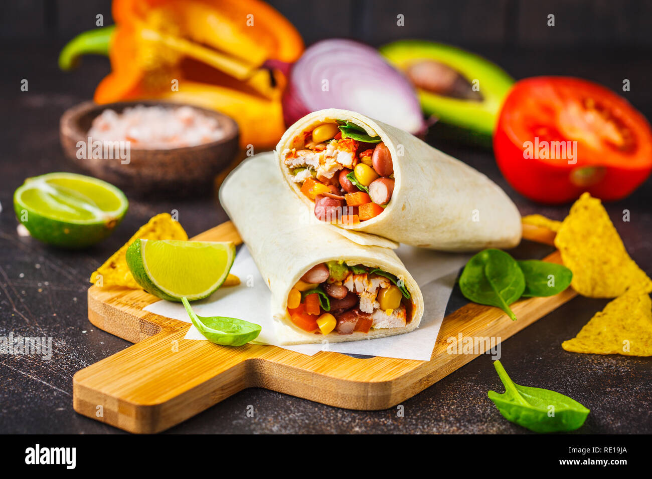 Burrito avvolge con pollo, fagioli, mais, pomodori e avocado su una tavola di legno, sfondo scuro. Carni burrito, cibo messicano. Foto Stock