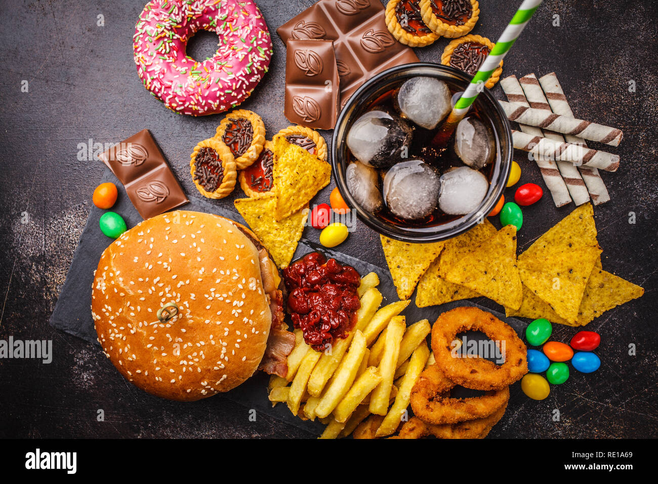 Junk food concept. Cibo malsano sfondo. Fast food e zucchero. Burger, dolci, patatine, cioccolato, ciambelle, soda su uno sfondo scuro. Foto Stock