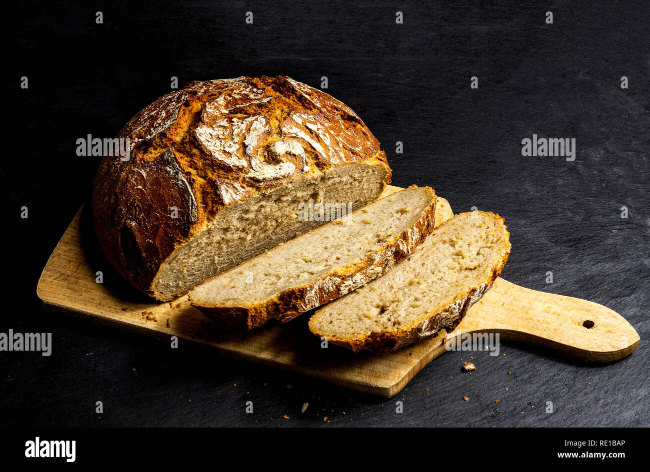 Fette di agricoltori tedeschi baurenbrot pane su una tavola di legno superficie con sfondo nero Foto Stock