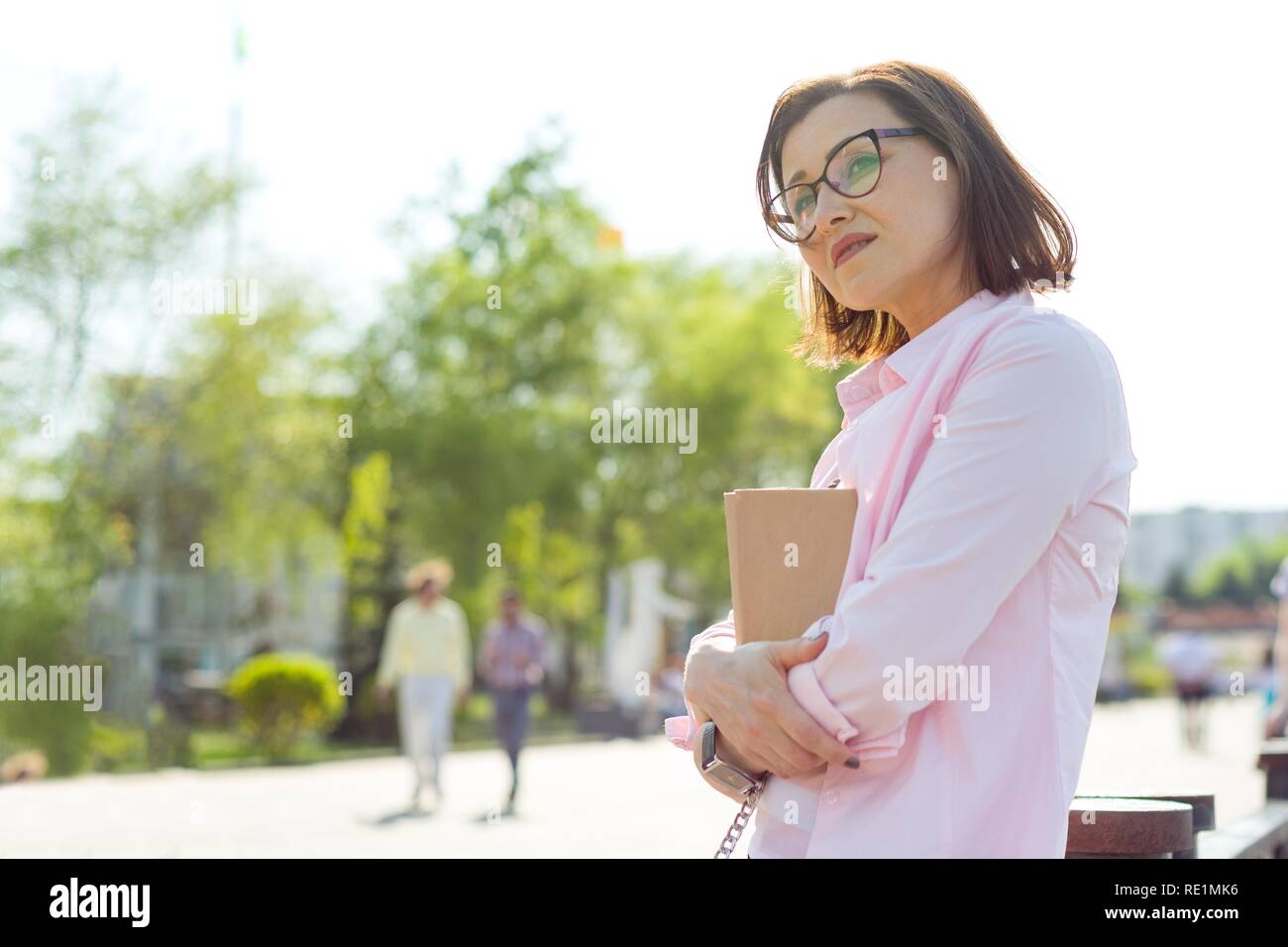 Ritratto Outdoor donna di mezza età. Background srteet, città, sul fiume. Tiene un libro, guarda a distanza, spazio di copia Foto Stock