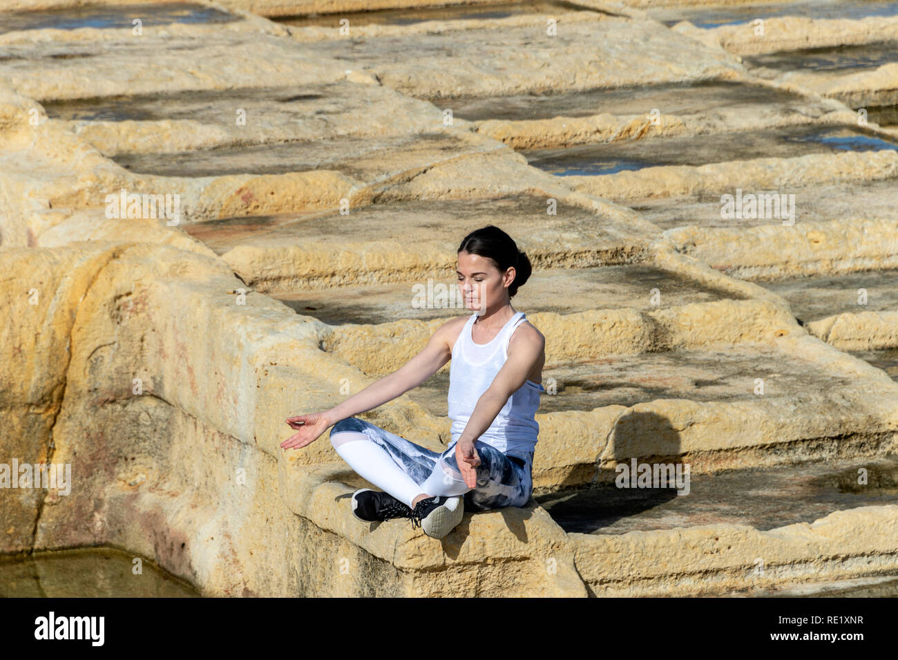 Donna meditando, seduto tra calcare le saline di Malta Foto Stock