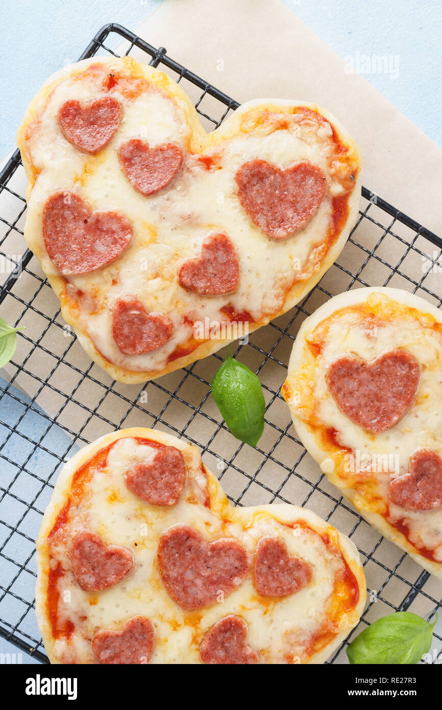 Mini pizza - freschi fatti in casa a forma di cuore mini pizza con salsiccia per pizza, formaggio, pomodori e basilico. Scatto dall'alto. Foto Stock