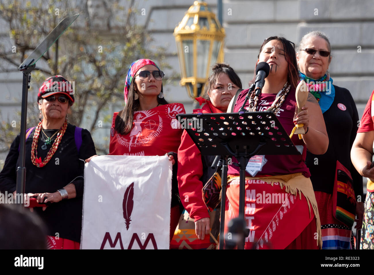 San Francisco, Stati Uniti d'America. 19 gennaio, 2019. Le donne di Marzo a San Francisco inizia con un rally al Civic Center Plaza di fronte al Palazzo del Municipio. Mancante e assassinato donne indigene fu un tema importante in marzo e rally. Un gruppo di nativi americani la donna vestita in rosso sono raccolte come il rally ha iniziato e inoltre hanno marciato per portare attenzione al problema nella California del Nord. Qui, la arist, autore e attivista Kanyon Sayers-Roods apre il rally con una canzone. Sayers-Roods è di Costanoan Ohlone e patrimonio Chumash, e il suo lavoro è stato presentato al Museo de Young e la Galleria Somarts. Credito: Foto Stock