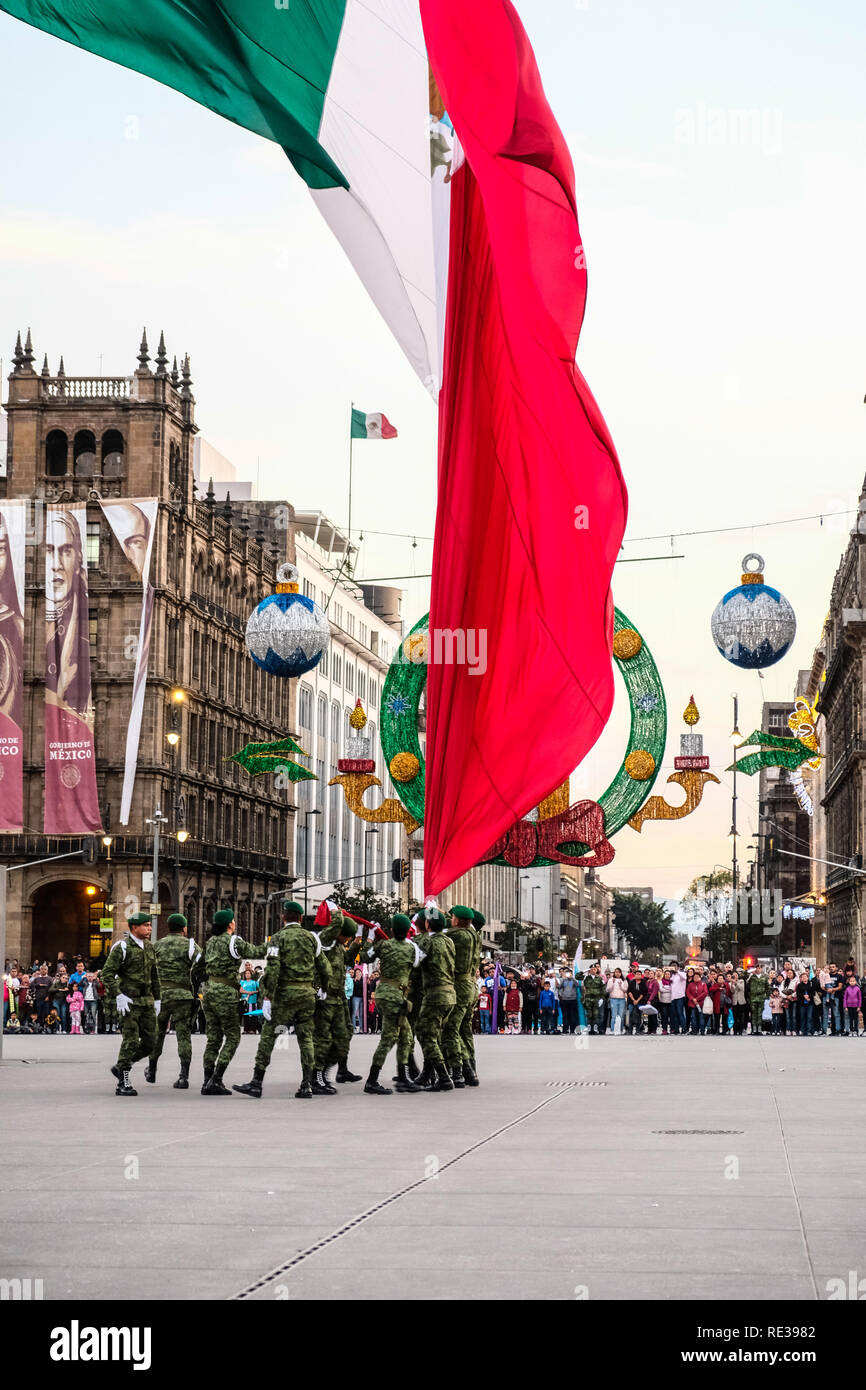La polizia militare cadre tenendo giù il Messico bandiera nazionale al Zocalo, Città del Messico, con la gente a guardare Foto Stock
