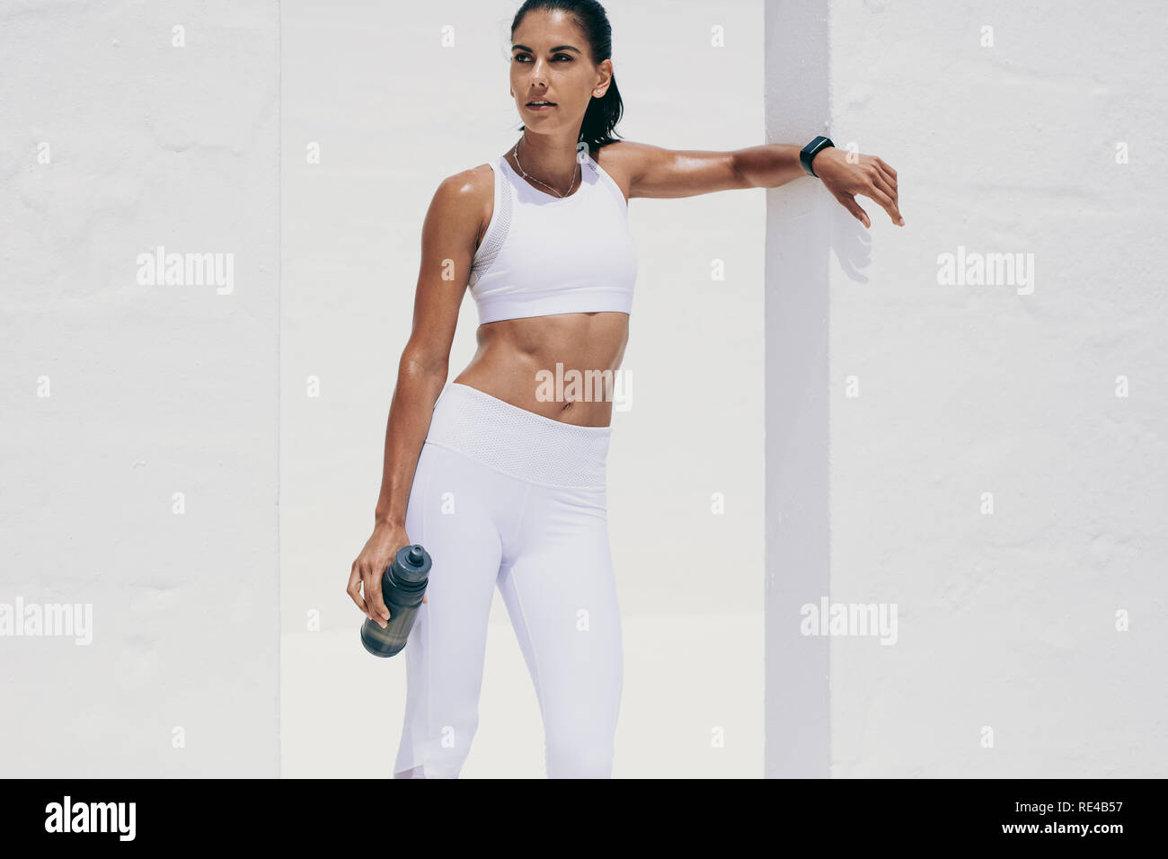 Donna in usura fitness prendendo una pausa da allenamento in piedi con una bottiglia di acqua in mano. Athletic donna prendendo una pausa di acqua durante l'allenamento. Foto Stock