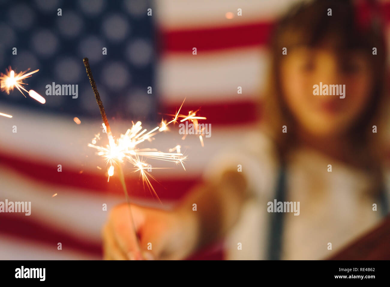 Kid celebrando indipendenza americana dal fuoco ardente brilla. Kid giocando con il fuoco brilla con la bandiera americana in background. Foto Stock