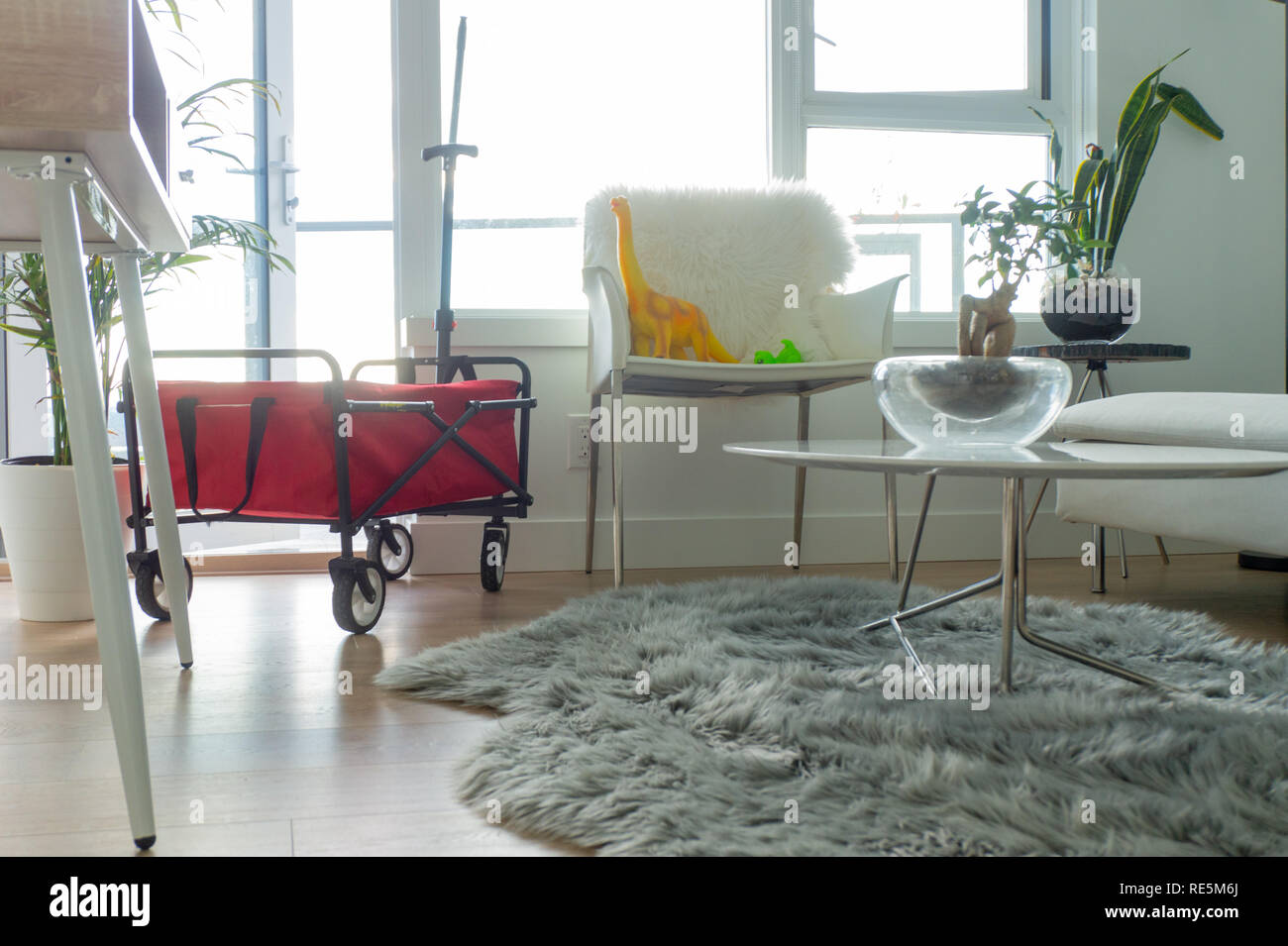 Rosso carro pieghevole in appartamento luminoso soggiorno, con giocattoli di dinosauro seduto su una sedia. Grigio con fodera in pelliccia sintetica tappeto sul pavimento. Foto Stock