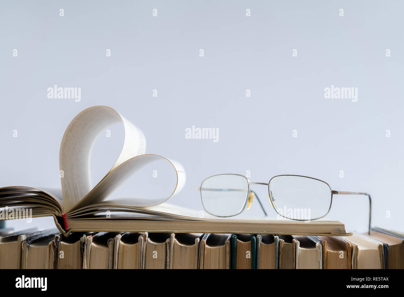 Vecchio hard cover pagina di libro decorare a forma di cuore con gli occhiali sul lato per amore il giorno di San Valentino con sfondo sfocato e copia di spazio per il testo. C Foto Stock