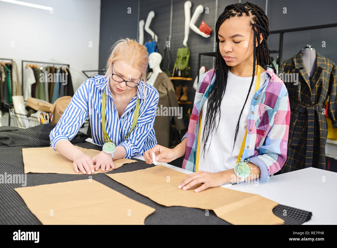 Due giovani designer di moda schizzi di disegno su tessuto insieme a sarti tabella in officina Foto Stock
