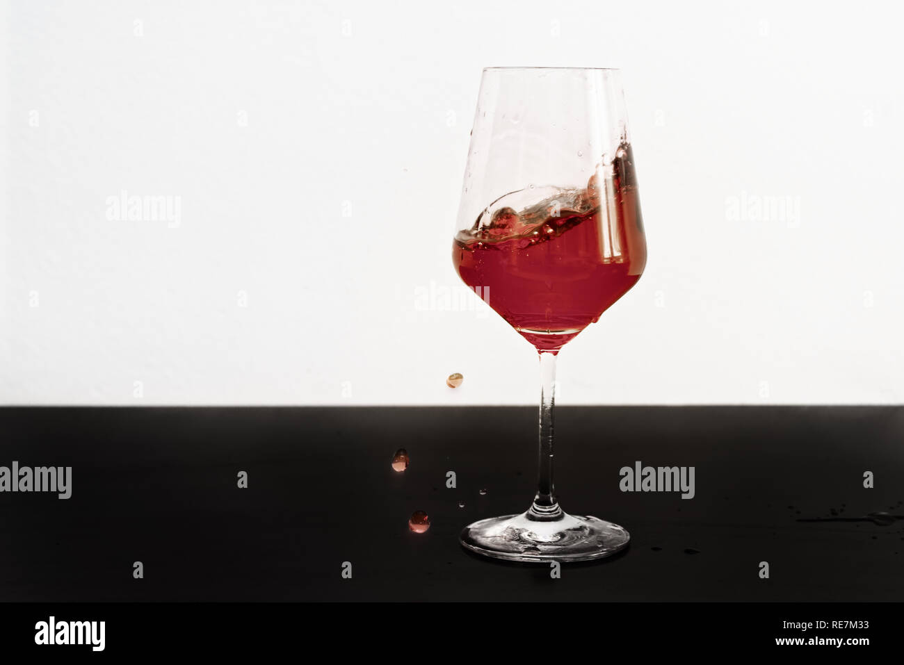 Bicchiere di vino sul tavolo scuro e sfondo bianco con vino rosso schizzi fuori di un vetro Foto Stock