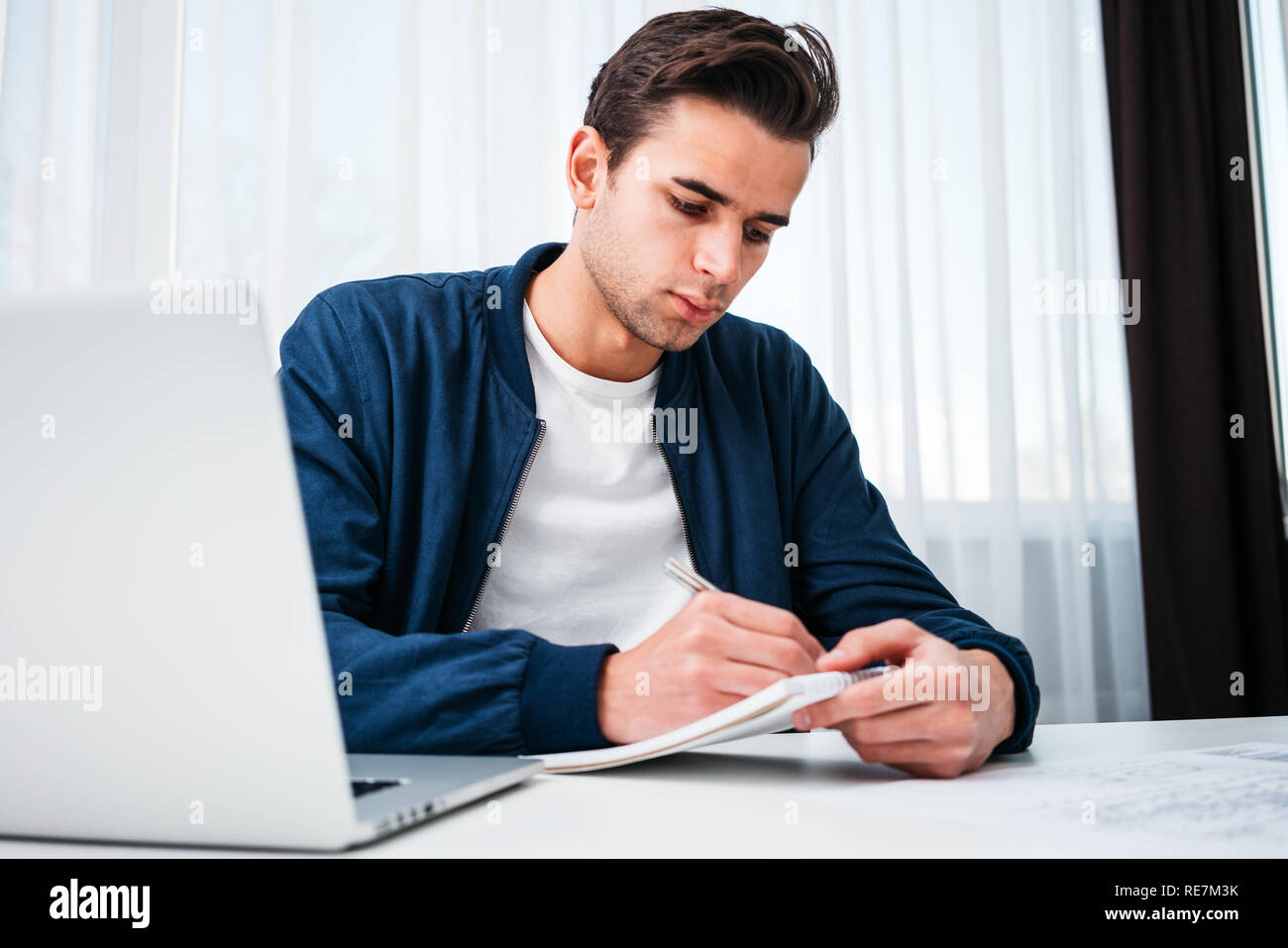 Uomo Barbuto utilizzando laptop e la preparazione del piano di progetto seduta a tavola la sua casa moderna. Concentrate l uomo la scrittura di nuove idee in notepad guardando sullo schermo Foto Stock