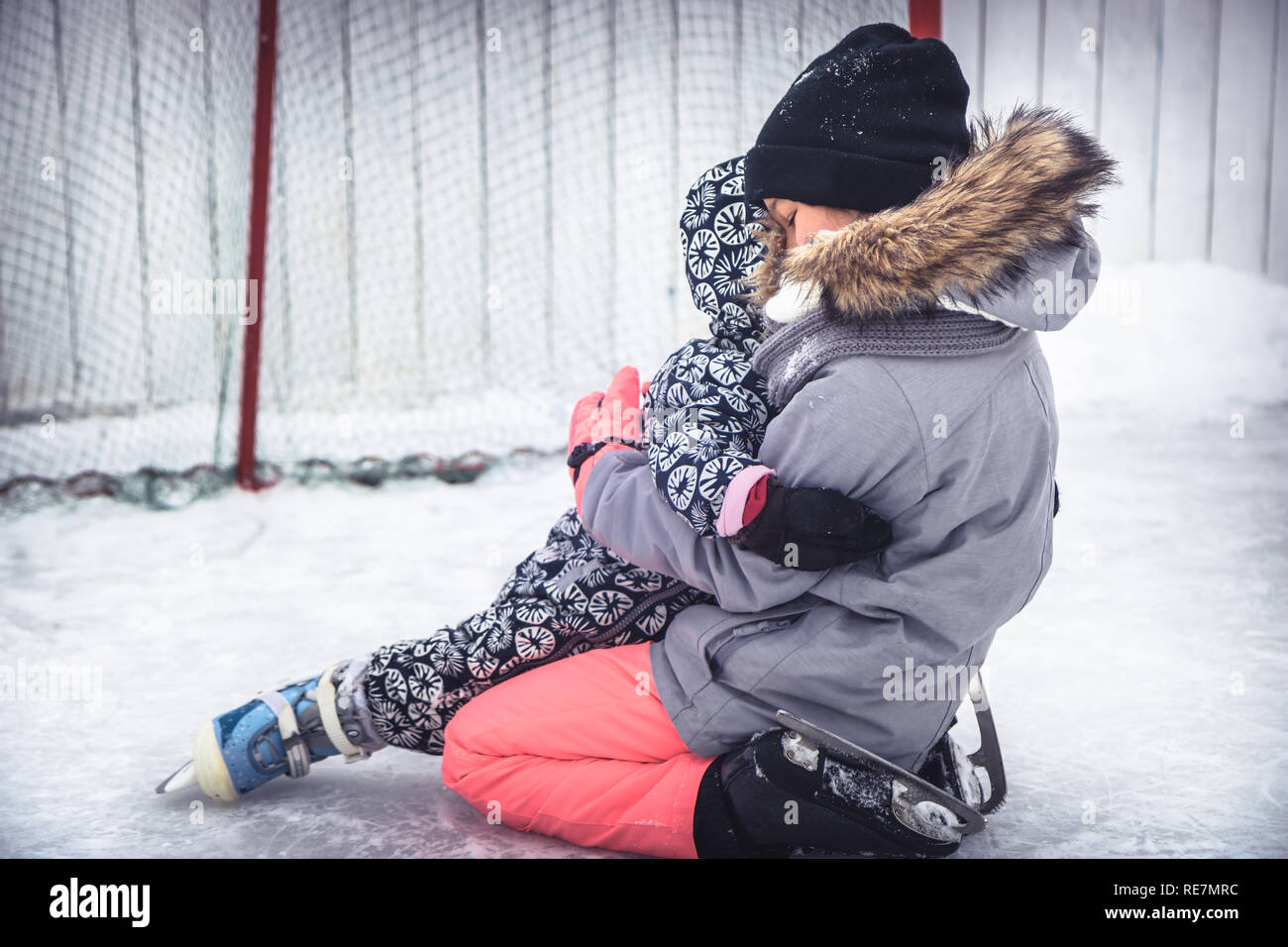 Bambino toddler rientrano in sambuco sorelle abbracciare quando l apprendimento pattinaggio sul ghiaccio sulla pista di pattinaggio superando difficoltà attraverso le lesioni in un parco di neve durante Foto Stock