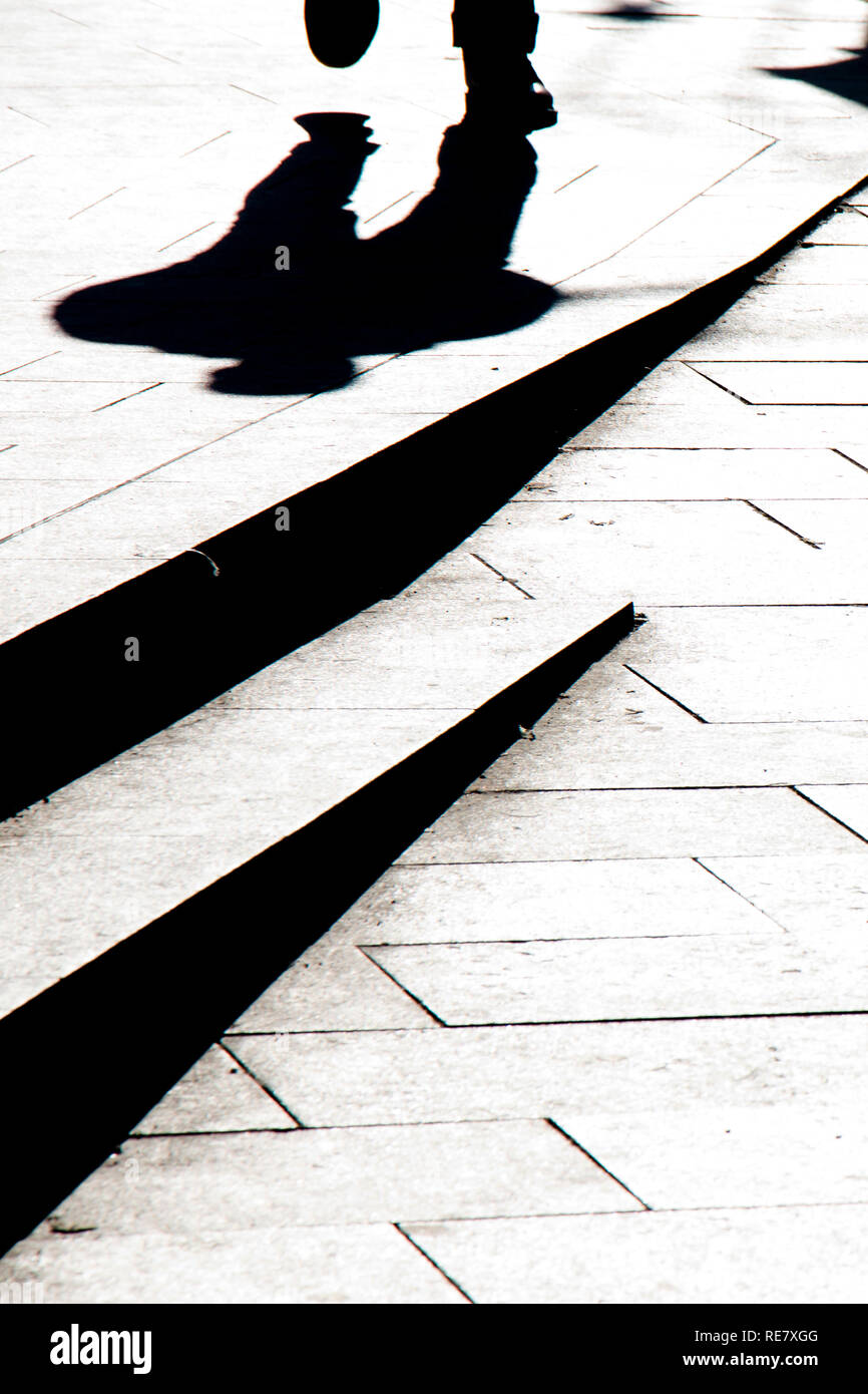 Silhouette sfocate ombra di un uomo che cammina su un marciapiede in città con gradini in bianco e nero a contrasto elevato Foto Stock