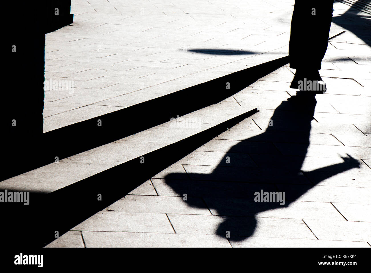 Silhouette sfocate ombra di un uomo che cammina su un marciapiede in città con gradini in inverno in bianco e nero a contrasto elevato Foto Stock