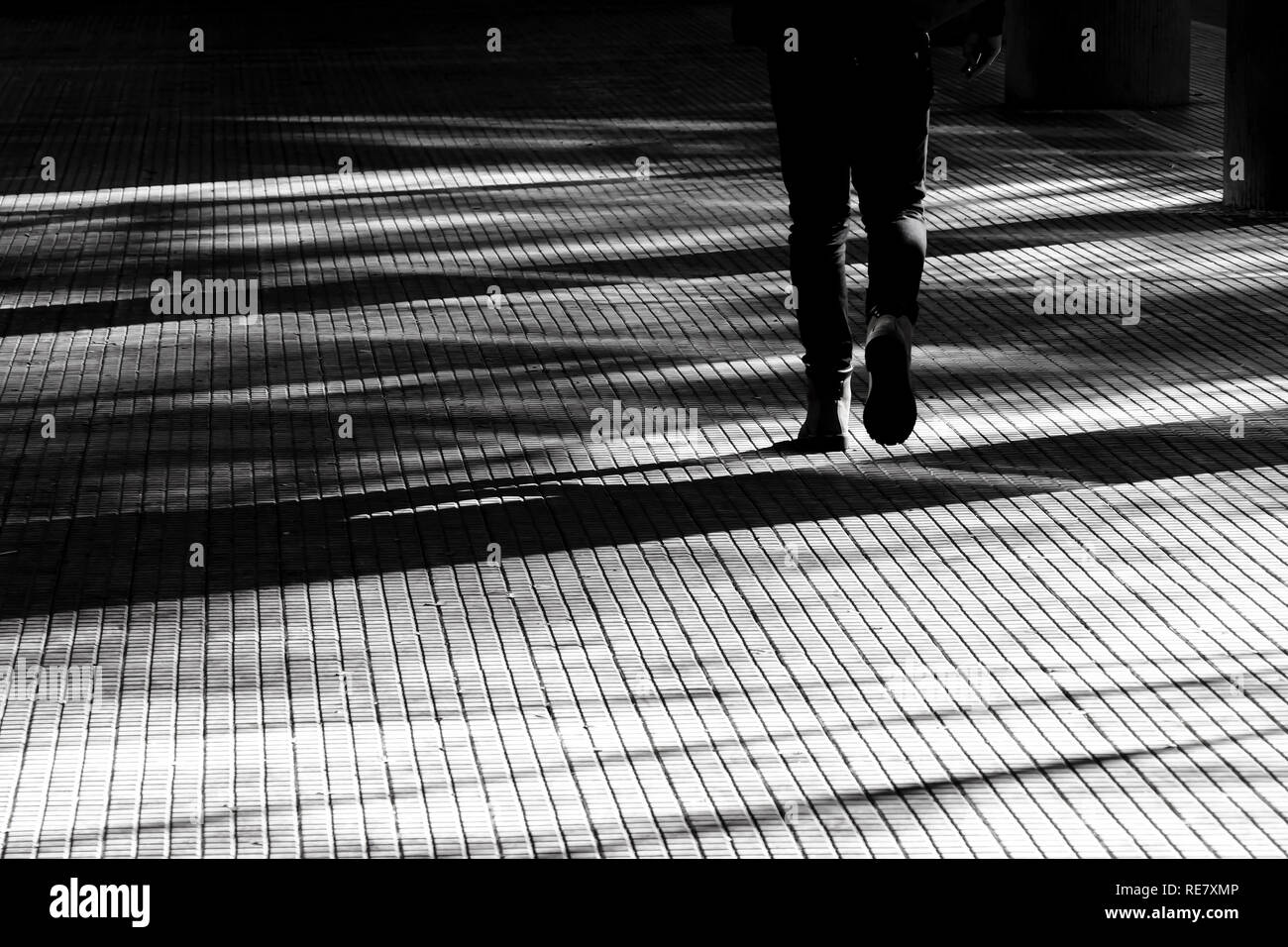 Silhouette sfocate ombra di gambe di una persona che cammina su una città arcade marciapiede in bianco e nero a contrasto elevato Foto Stock