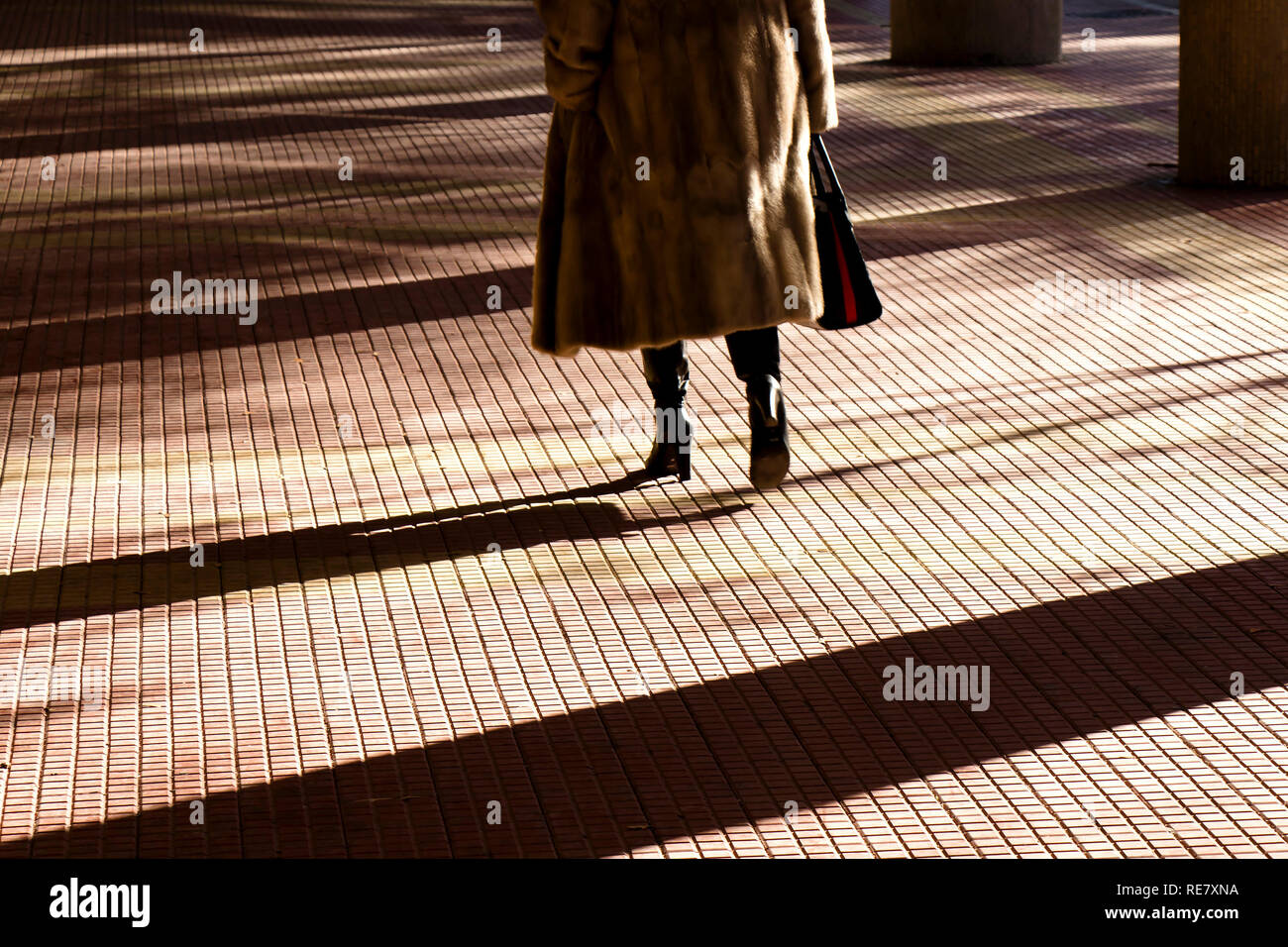 Silhouette sfocate ombra delle gambe di una donna in pelliccia e tacchi alti e stivali a camminare su una città arcade sun passerella illuminata Foto Stock