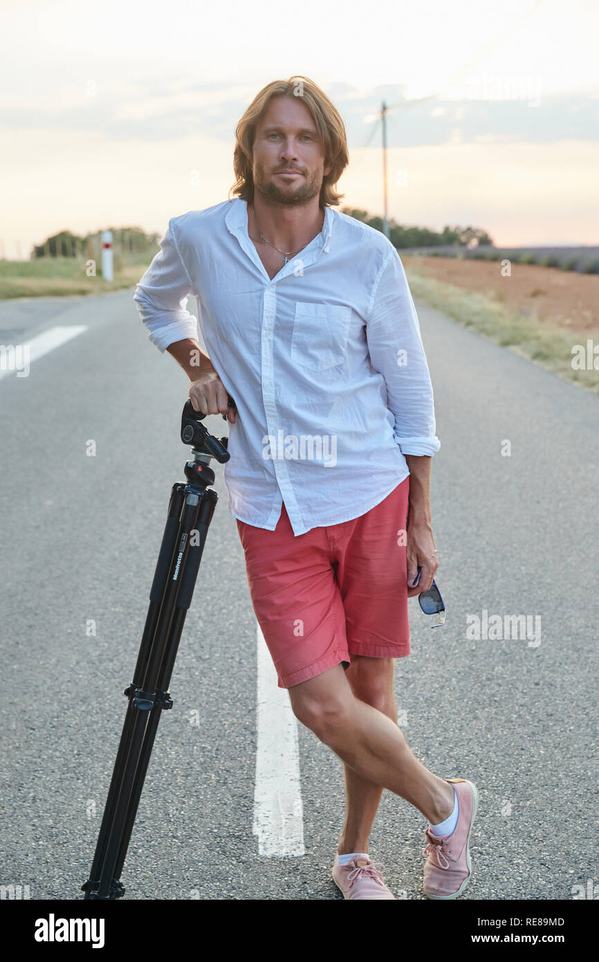 La bellissima giovane uomo brutale sorge sulla strada al tramonto, egli è  vestito con una camicia bianca con maniche corte e pantaloncini rossi, il  fotografo Foto stock - Alamy
