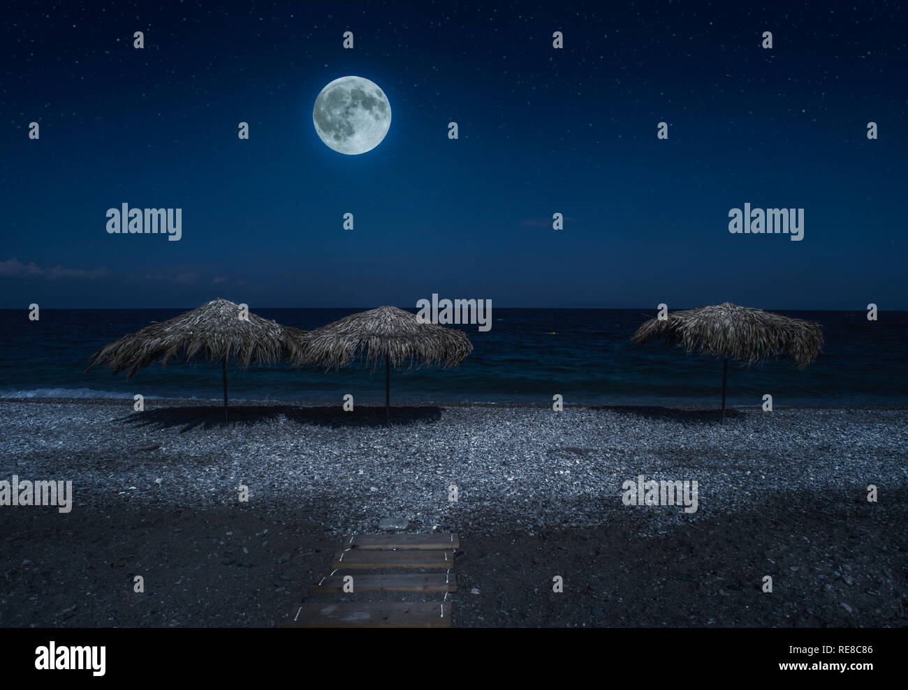 Ombrelloni di paglia sulla spiaggia di notte. Chiaro di luna sul mare. Notte cielo stellato. Foto Stock