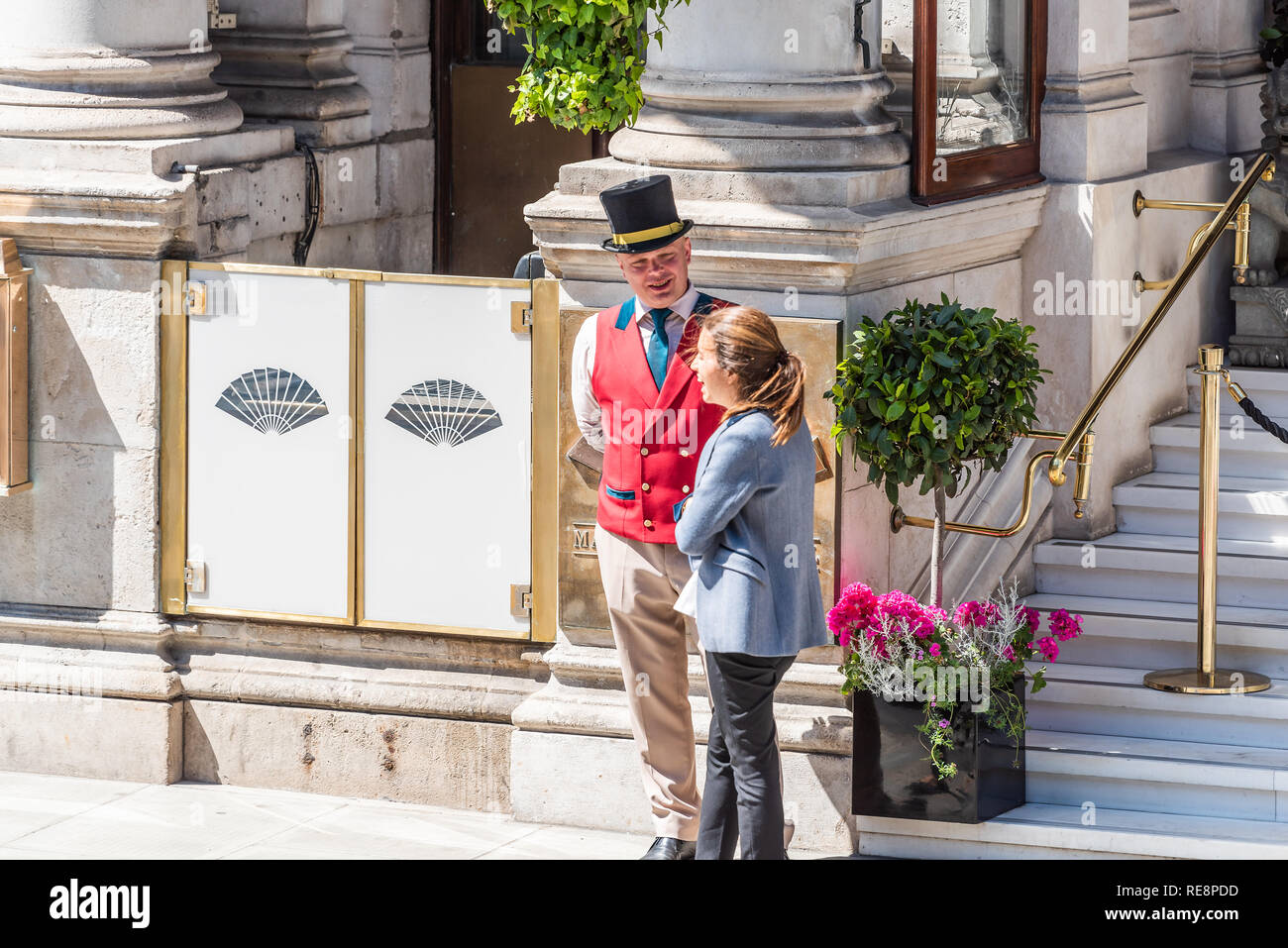 London, Regno Unito - 22 Giugno 2018: Porter portiere in abito tradizionale abbigliamento e cappello con gilet rosso in piedi a parlare al turista da ingresso a Manda Foto Stock