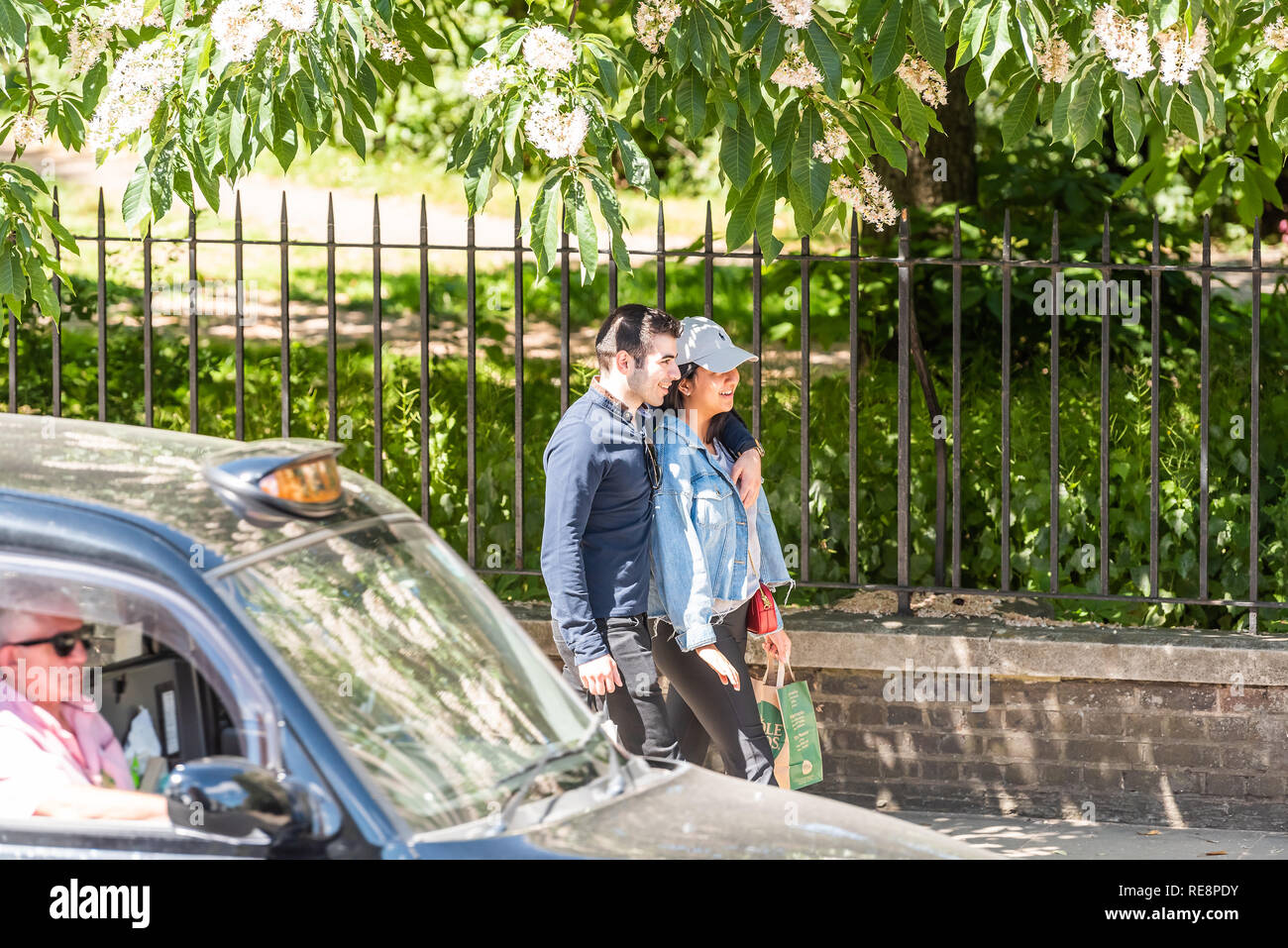 London, Regno Unito - 22 Giugno 2018: due persone coppia giovane ridere sorridere i pedoni a camminare sul marciapiede strada durante la soleggiata giornata estiva da Hyde park Foto Stock
