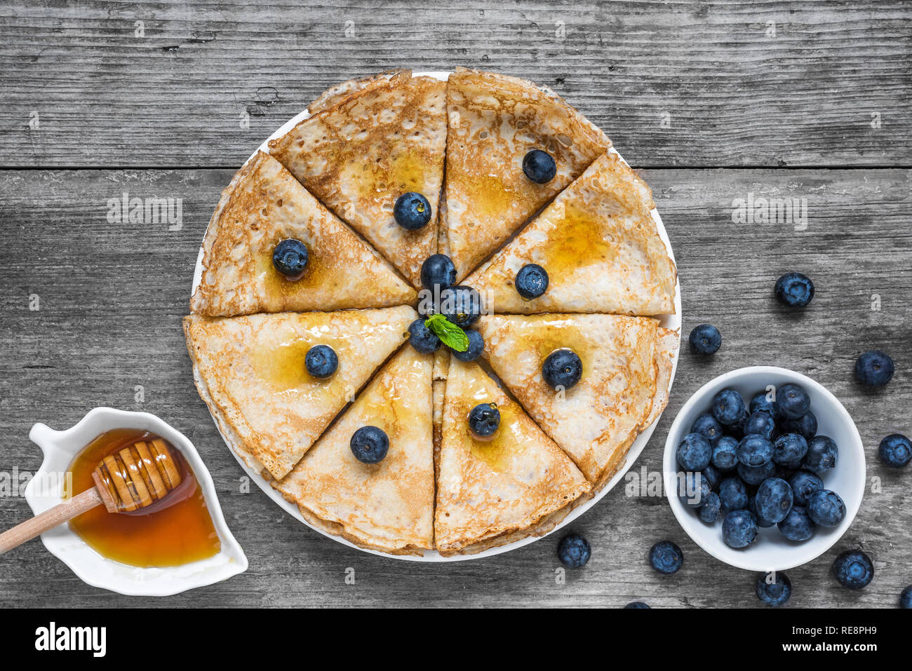 Crepes fatte in casa servite con mirtilli freschi, sciroppo di acero o miele e menta su tavola in legno rustico. vista superiore Foto Stock