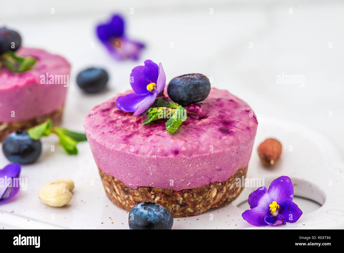 Mirtillo e acai vegane anacardi dolci con frutti di bosco freschi, fiori commestibili, menta, dadi. sano cibo vegan concetto. close up Foto Stock