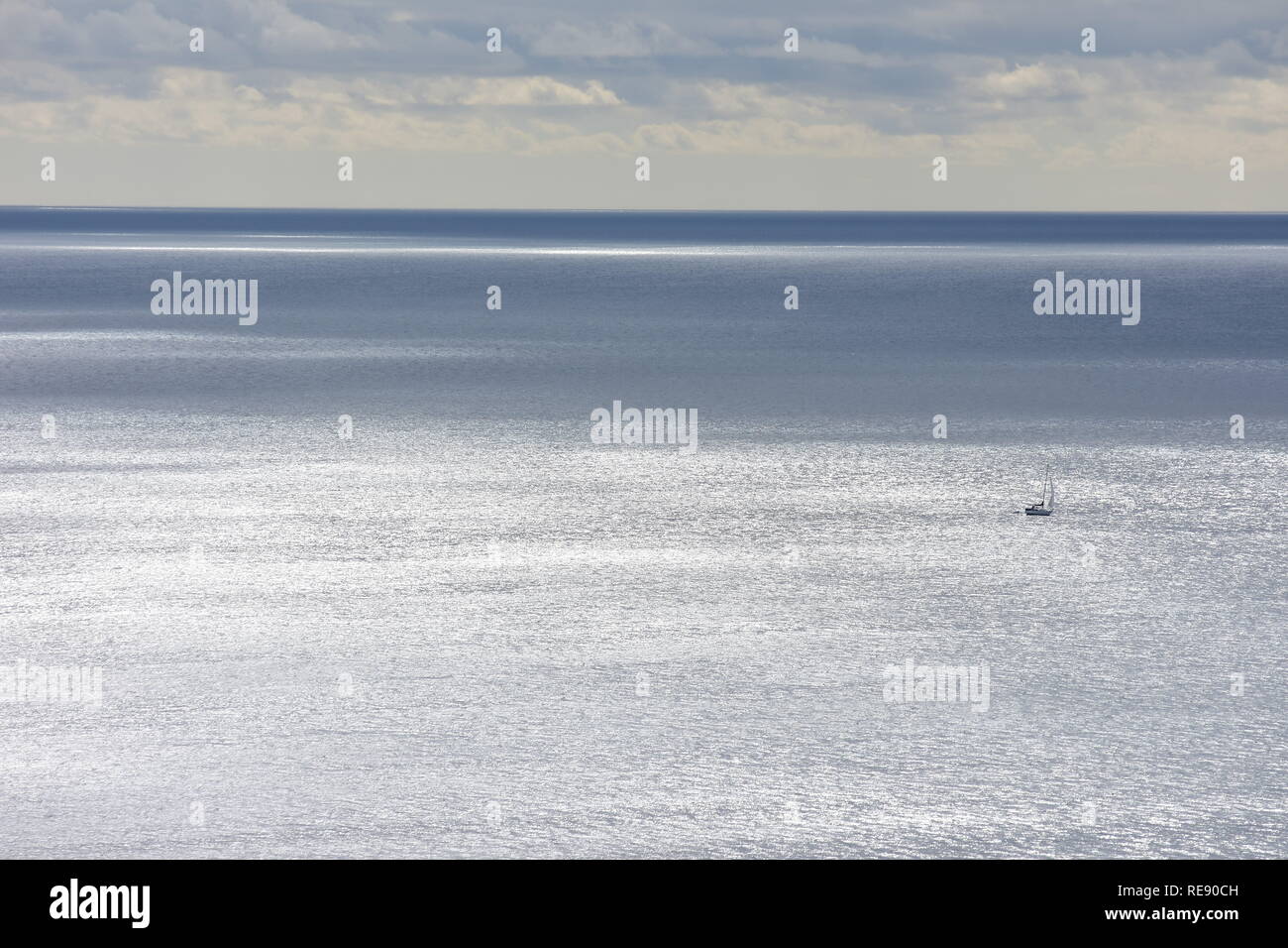Vista della superficie del mare che cambia colore da argento a grigio scuro con lone piccolo veliero essendo solo piccoli spot nel vasto oceano. Foto Stock