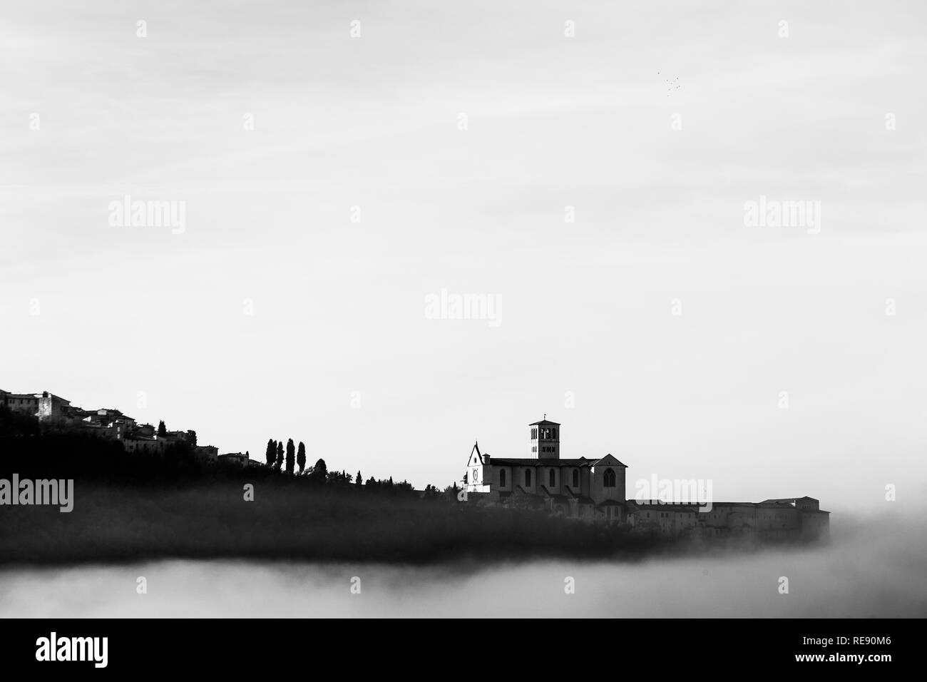Una vista della Basilica di San Francesco in Assisi nel mezzo della nebbia sotto un cielo profondo con le nuvole Foto Stock