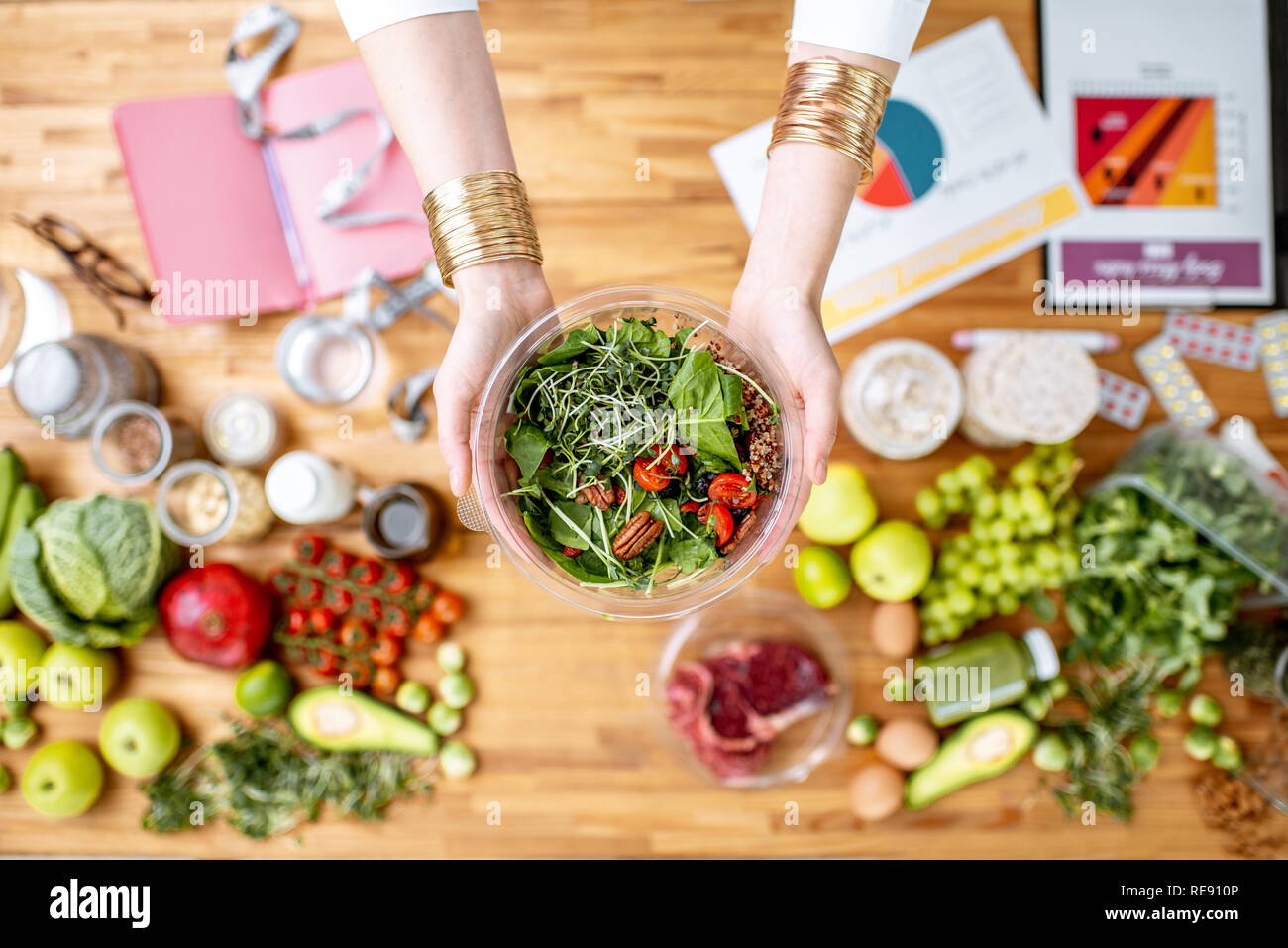 Dietista azienda insalata cotta sopra il tavolo pieno di vari prodotti sani e disegni sul tema del mangiare sano Foto Stock