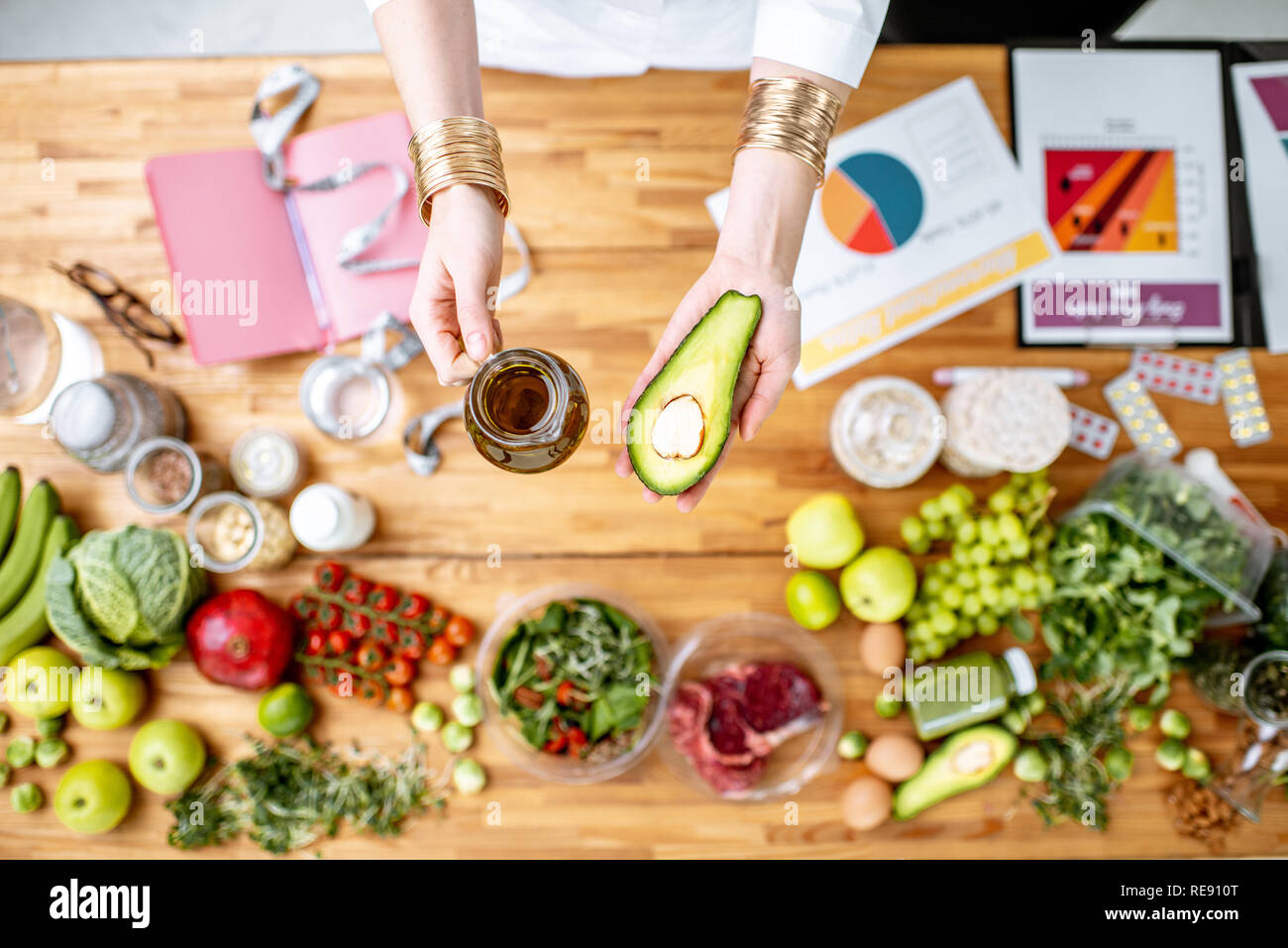 Dietista azienda avocado e olio d'oliva sopra il tavolo pieno di vari prodotti sani, dieta ketogenic concept Foto Stock