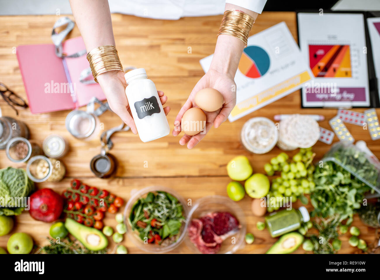 Dietista tenendo il latte e le uova sopra il tavolo pieno di vari prodotti sani e disegni sul tema del mangiare sano Foto Stock