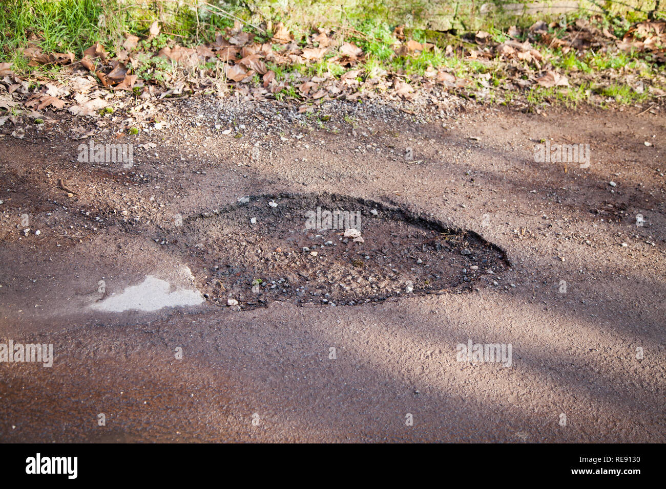 Buca nel paese strada nella campagna inglese. Strada asfaltata che necessitano di riparazione, la guida pericolosa superficie. Foto Stock