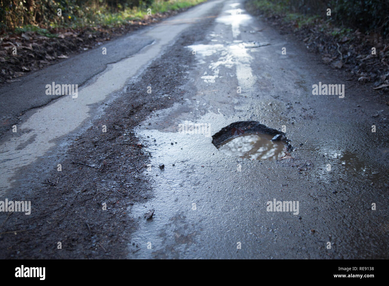 Buca nel paese strada nella campagna inglese. Strada asfaltata che necessitano di riparazione, la guida pericolosa superficie. Foto Stock