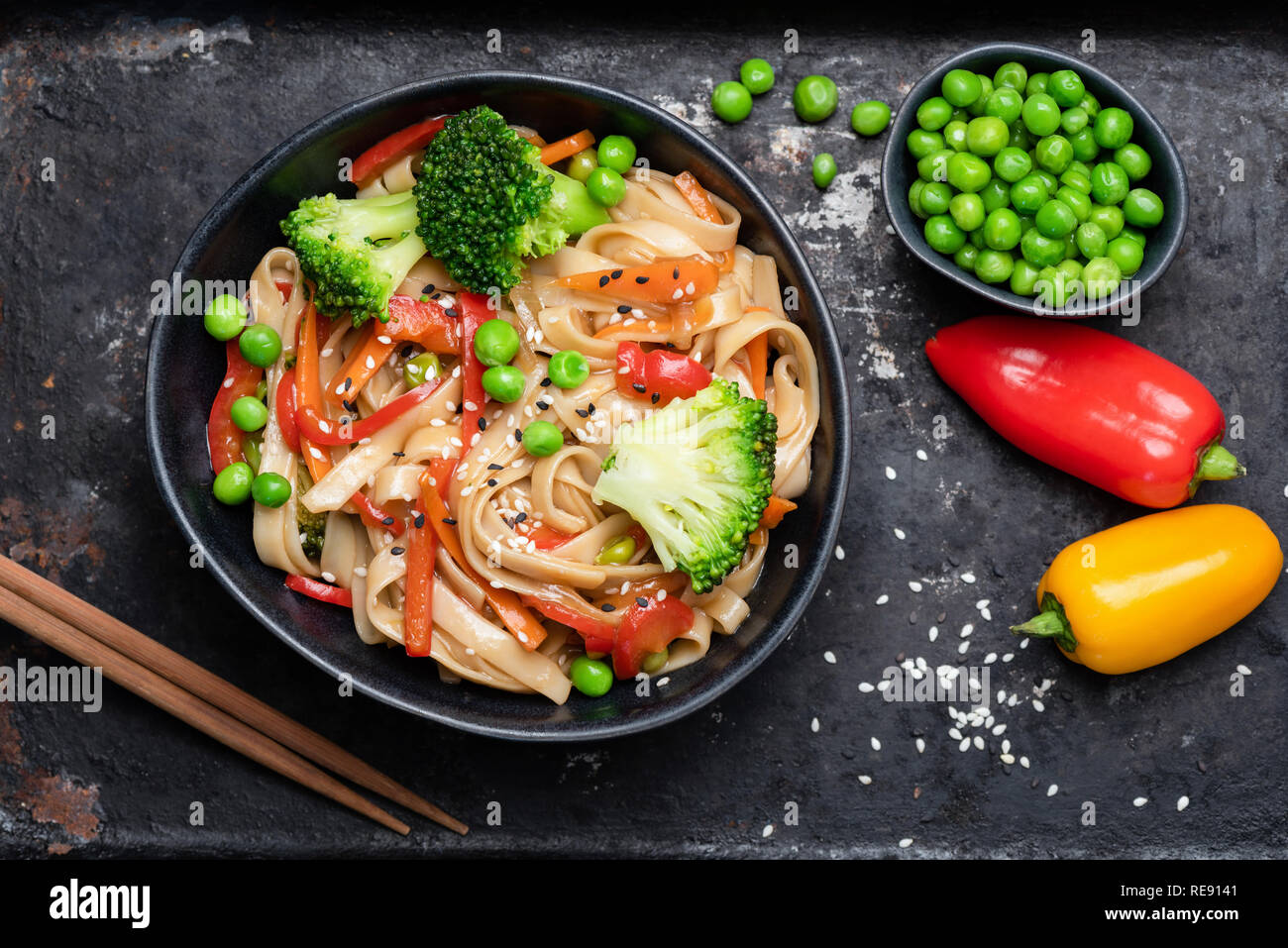 Asian stir fry con udon tagliatelle e verdure. Broccoli, verde pisello, pepe, carote e pasta in bianco e nero ciotola. Vista superiore Foto Stock